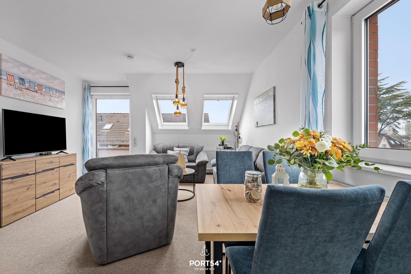 Wohn- und Essbereich mit TV, Sofa, Tisch und Stühlen. Fenster mit Blick nach außen.