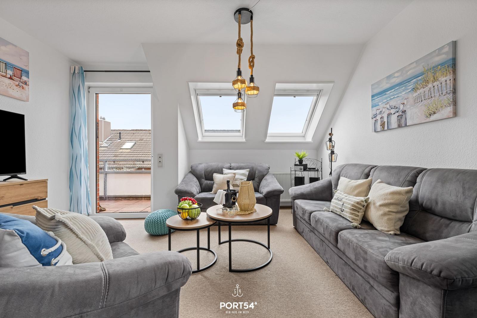 Wohnzimmer mit grauen Sofas, runden Tischen und Dachfenstern. Balkon und Wandbilder sichtbar.