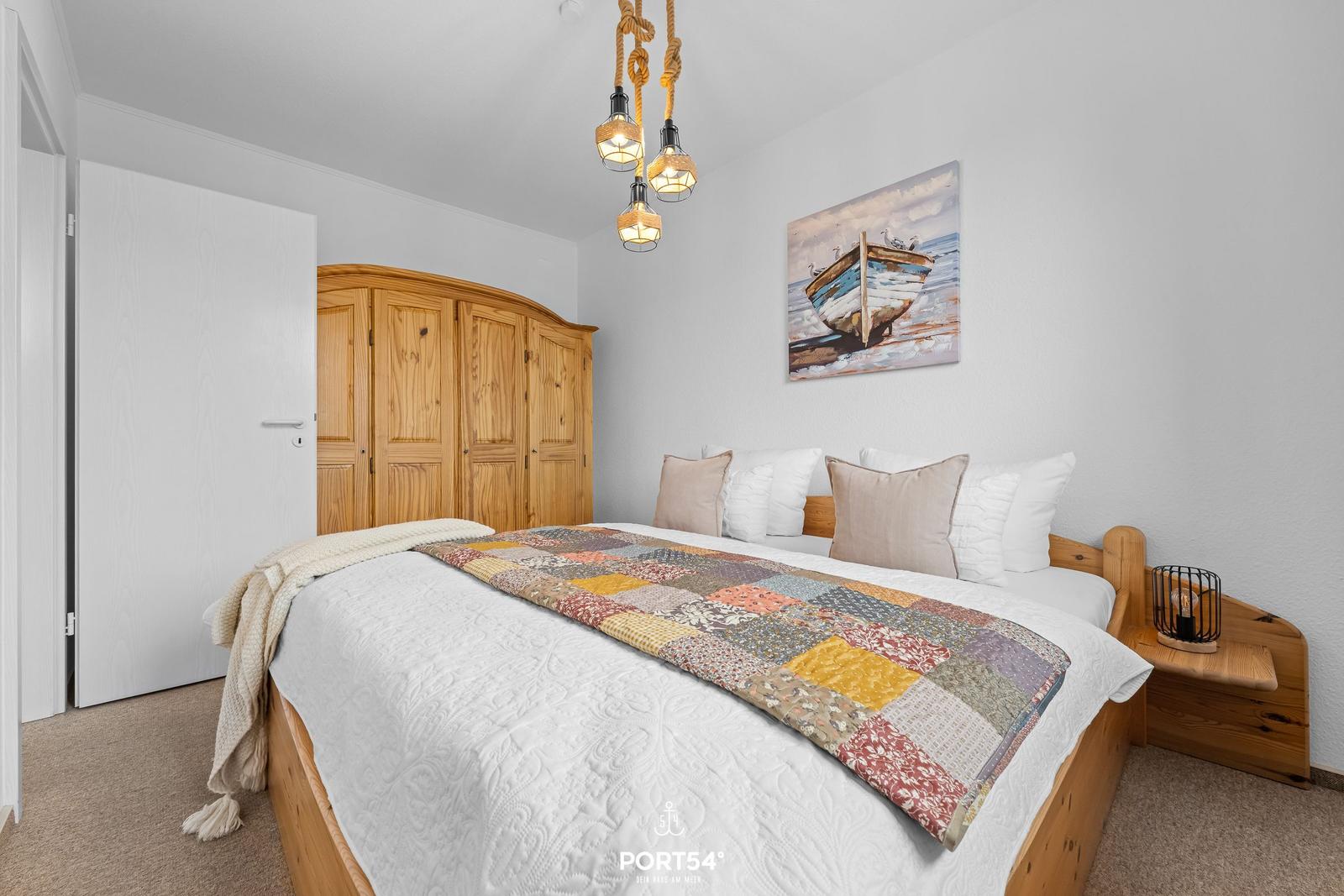 Schlafzimmer mit Holzbett, Kleider schrank und Wandbild mit Boot.