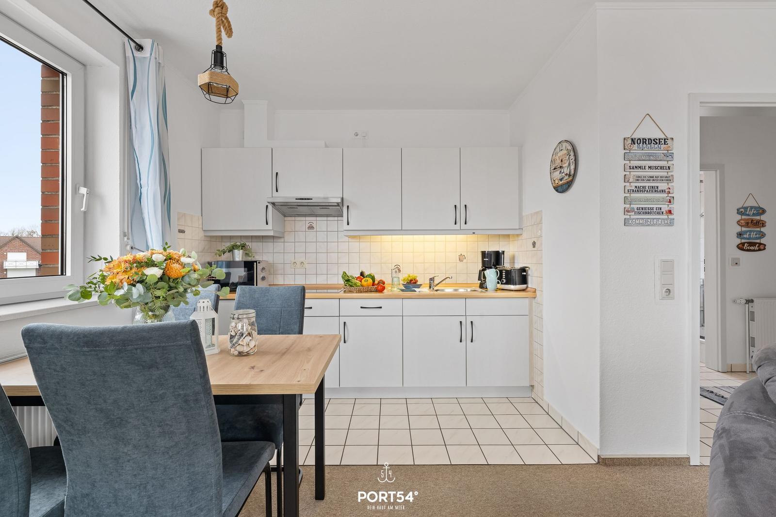 Küche mit Esstisch, weißen Schränken und Fenster. Wanddekoration und Küchenzeile sichtbar.