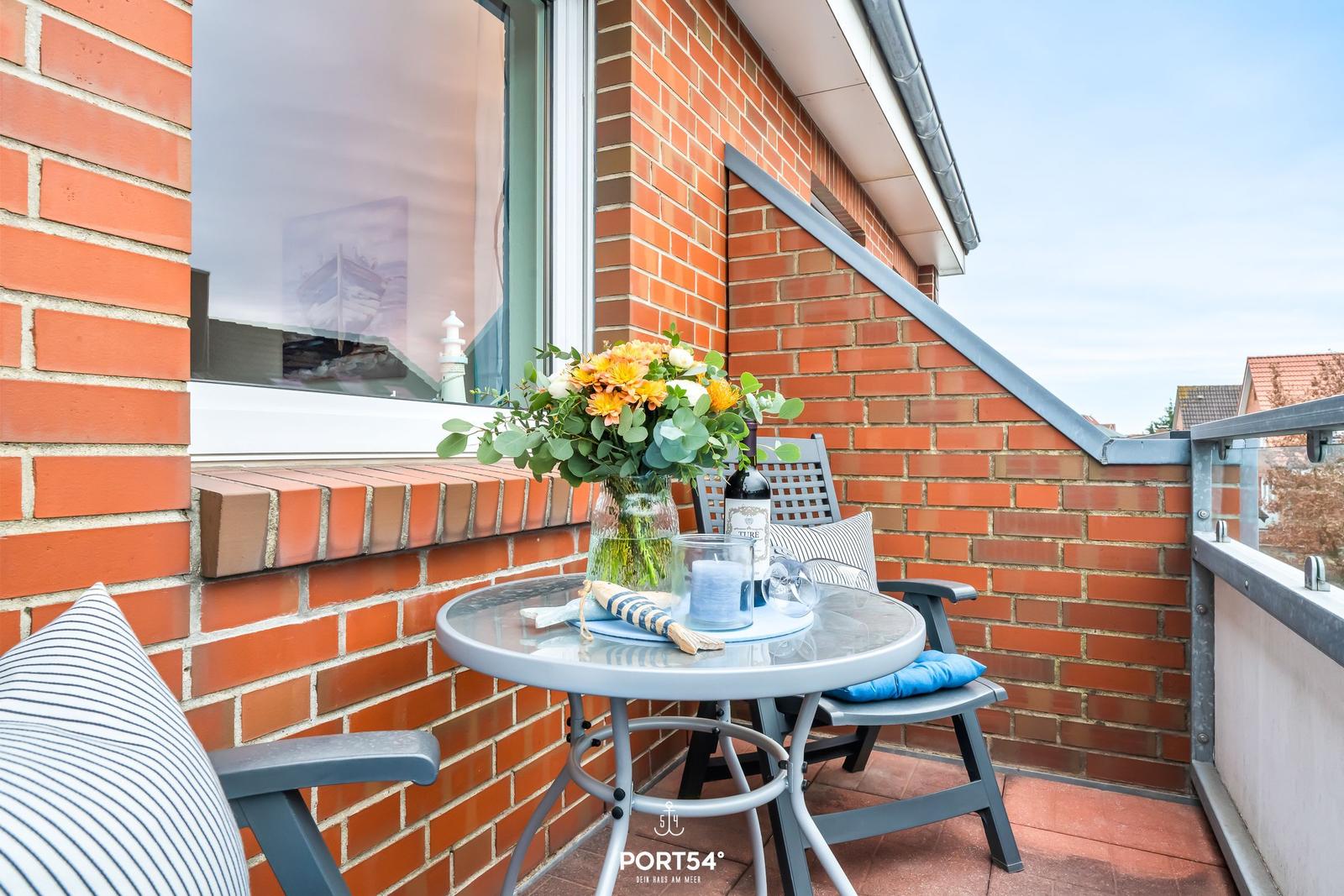 Balkon mit Tisch, Stühlen und Blumenvase an roter Ziegelwand.