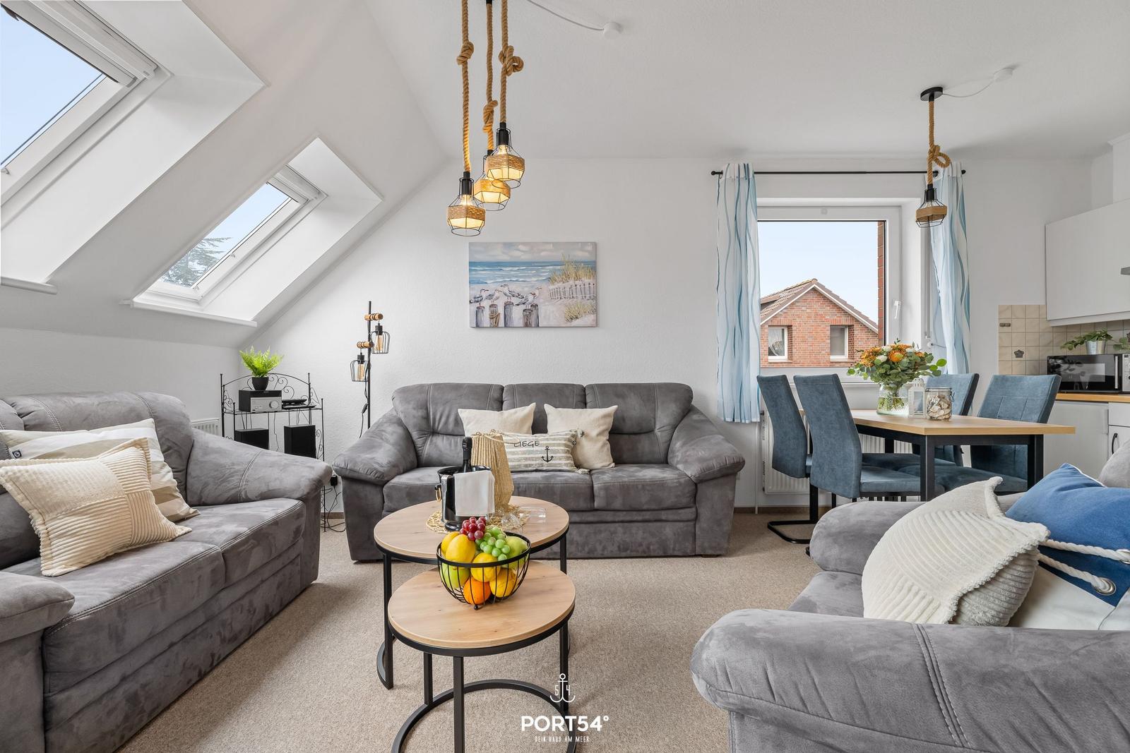 Wohnbereich mit grauen Sofas, Esstisch und Dachfenstern. Wandbild und Hängelampen.