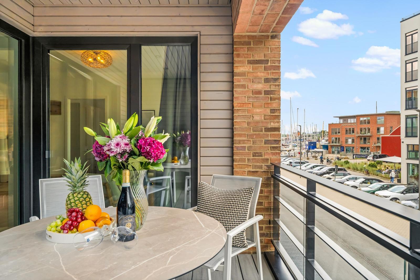 Terrace with table, chairs, and flowers. View of harbor and buildings.