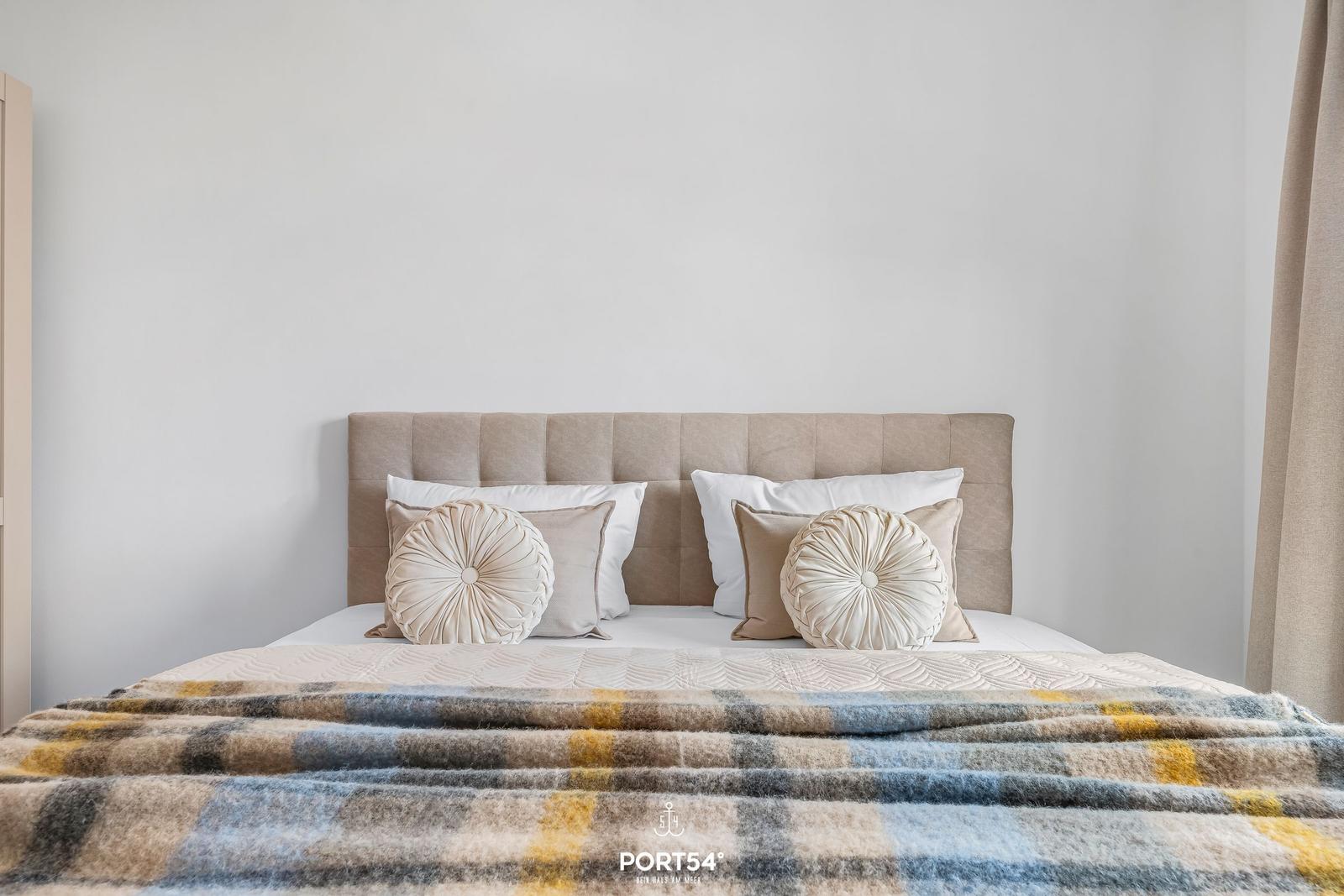 A bed with pillows and a blanket against a white wall.