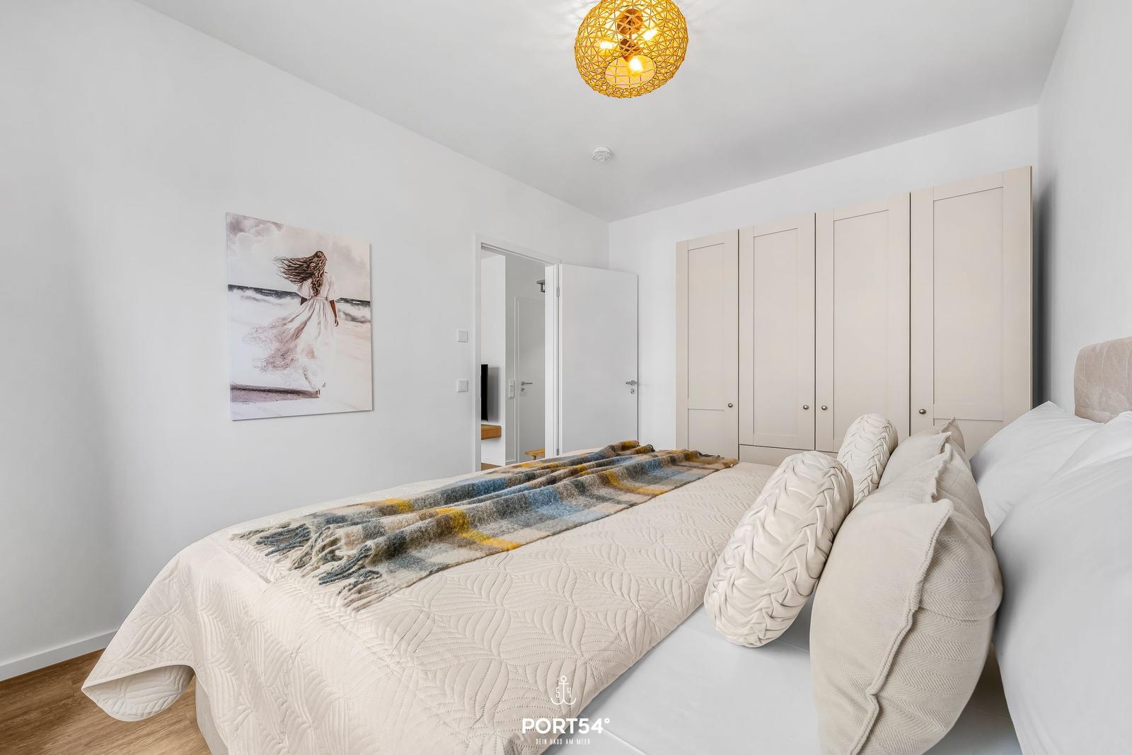 Bedroom with bed, wardrobe, and wall art. Ceiling light and wooden floor.