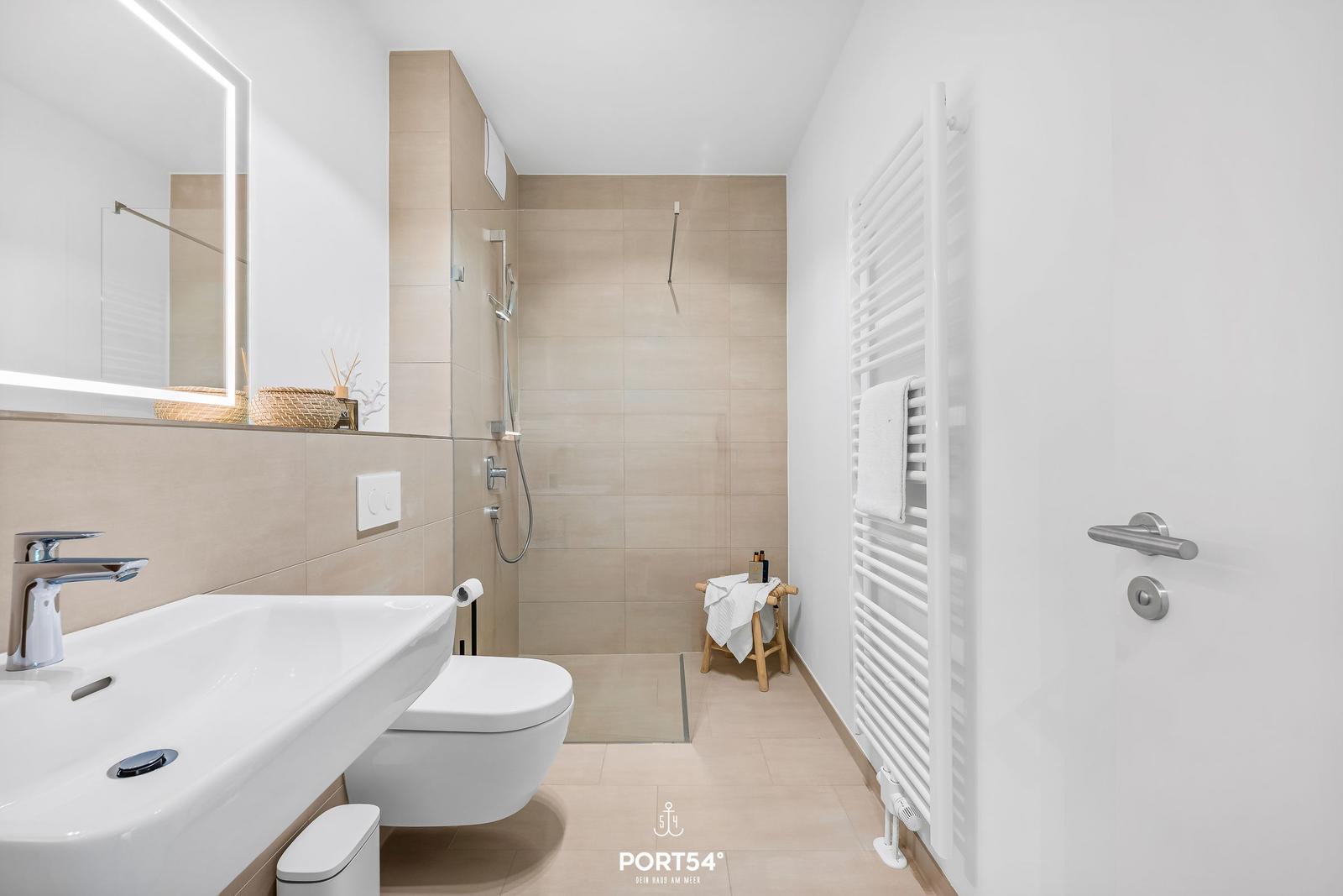 Bathroom with shower, sink, and toilet. White tiles and modern fixtures.