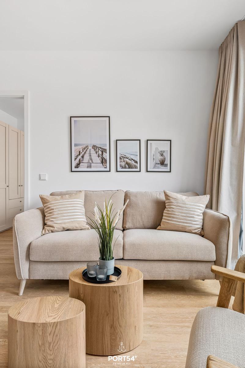 A living room with a sofa, two round wooden tables, and three wall pictures.