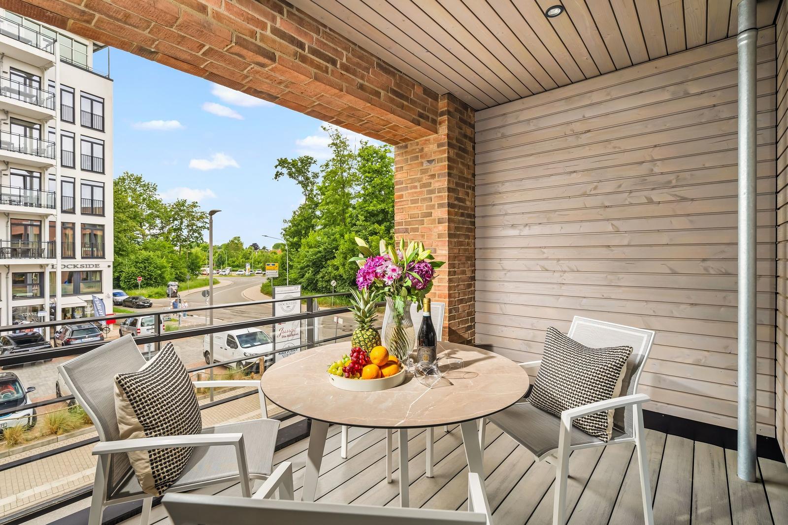 Terrace with table, chairs, and fruit. View of street and trees.