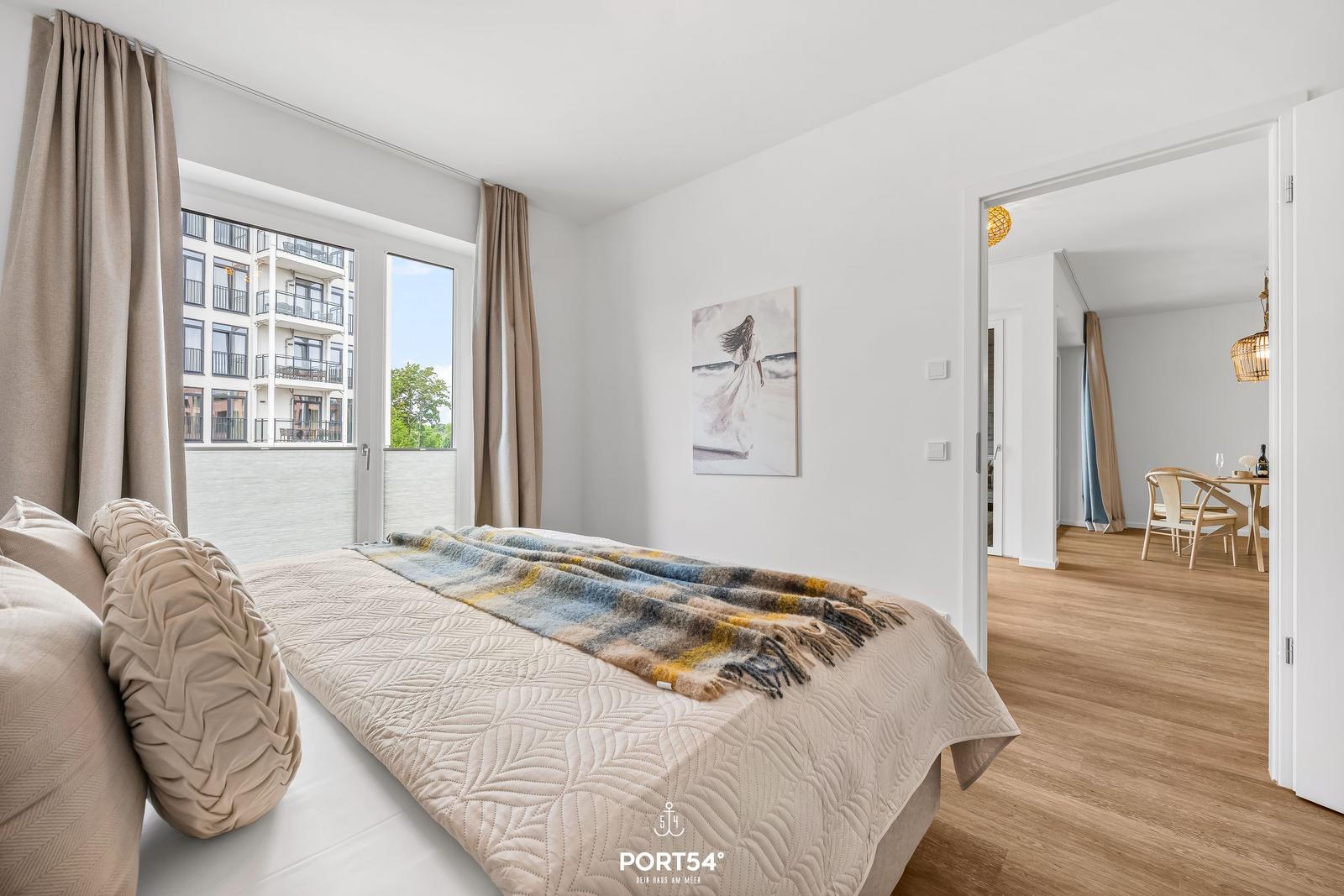 Bedroom with bed, window, and view of buildings. Passage to living area with dining table.