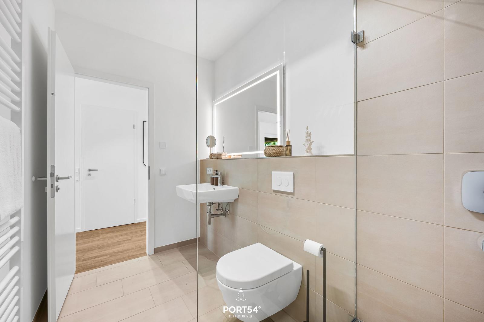 Bathroom with shower, toilet, and sink. Mirror with lighting and heater visible.