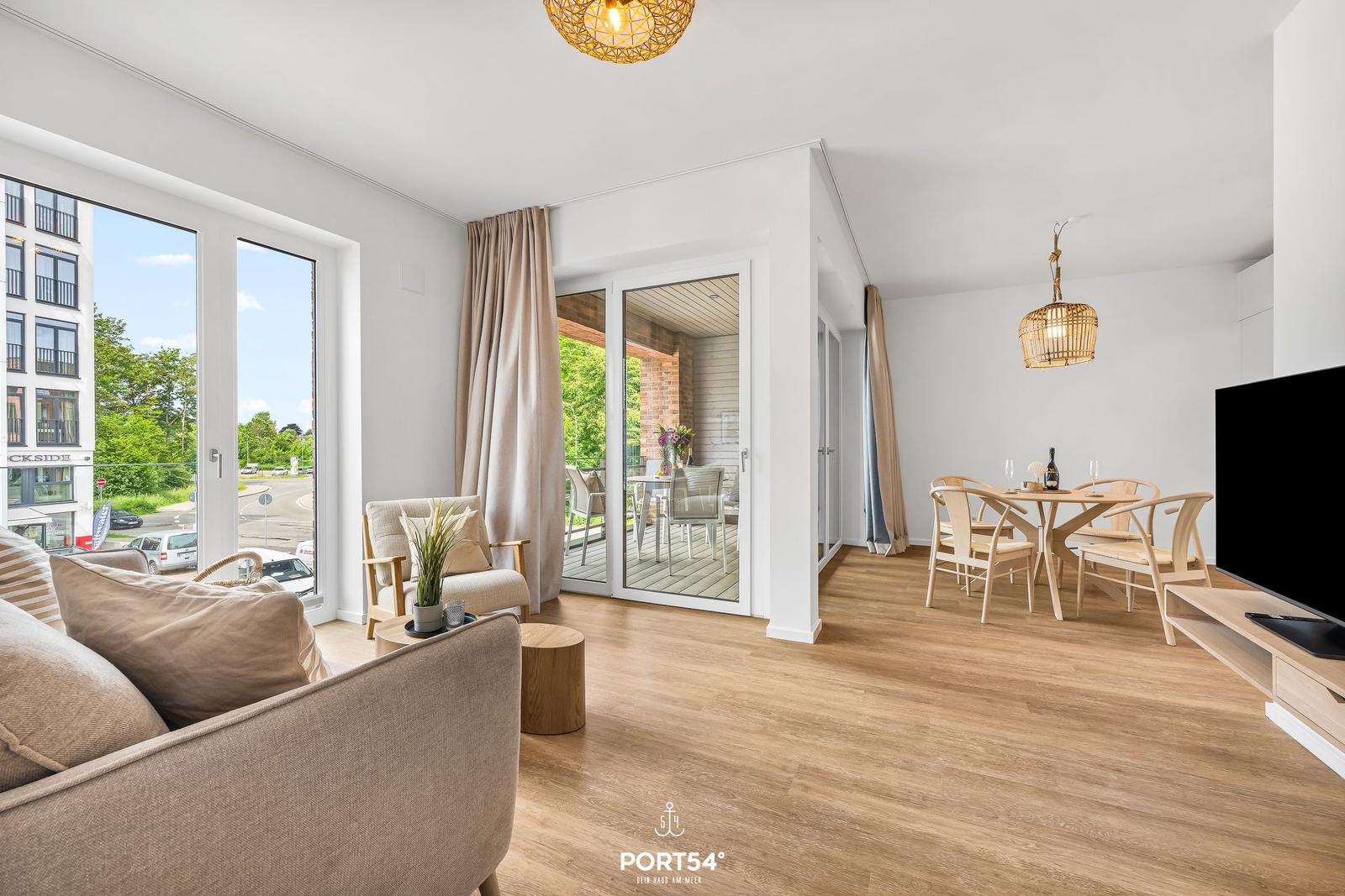 Living and dining area with wooden floor, seating, and view of balcony and street.