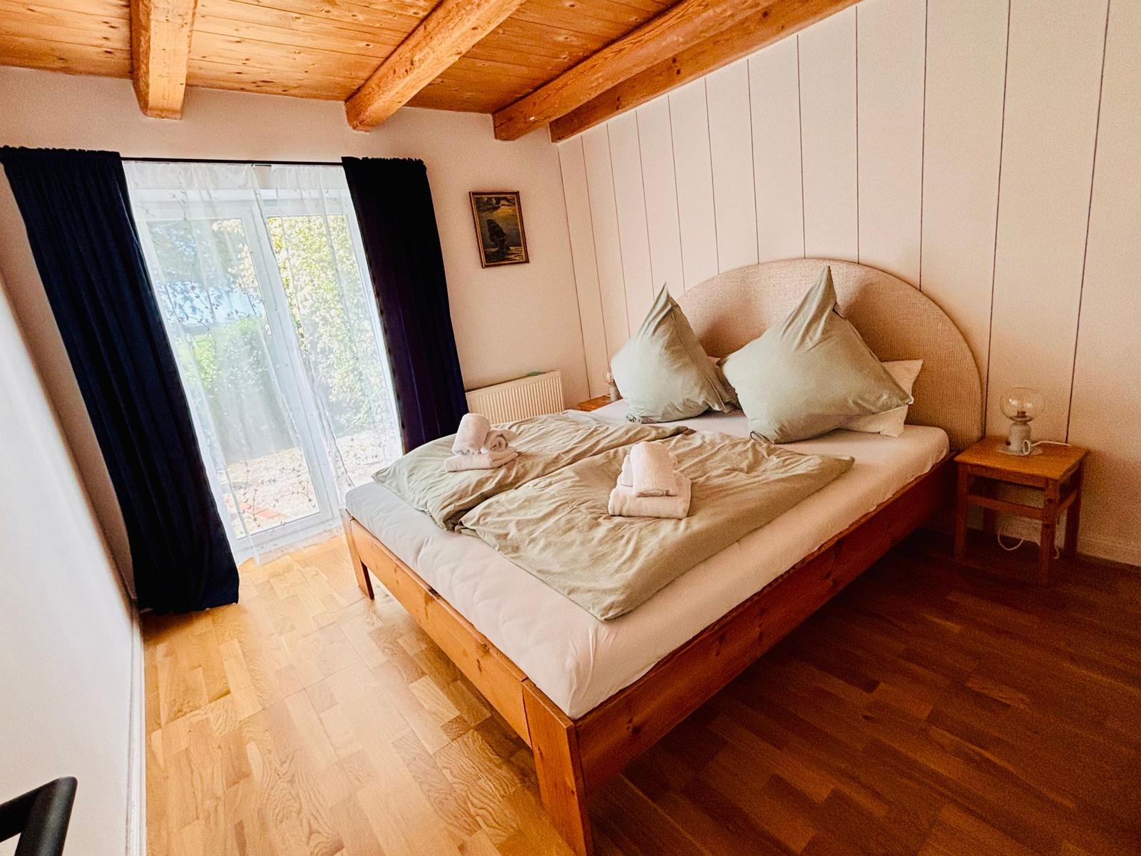 Schlafzimmer mit Holzboden, Bett und Fenster mit Blick nach draußen.