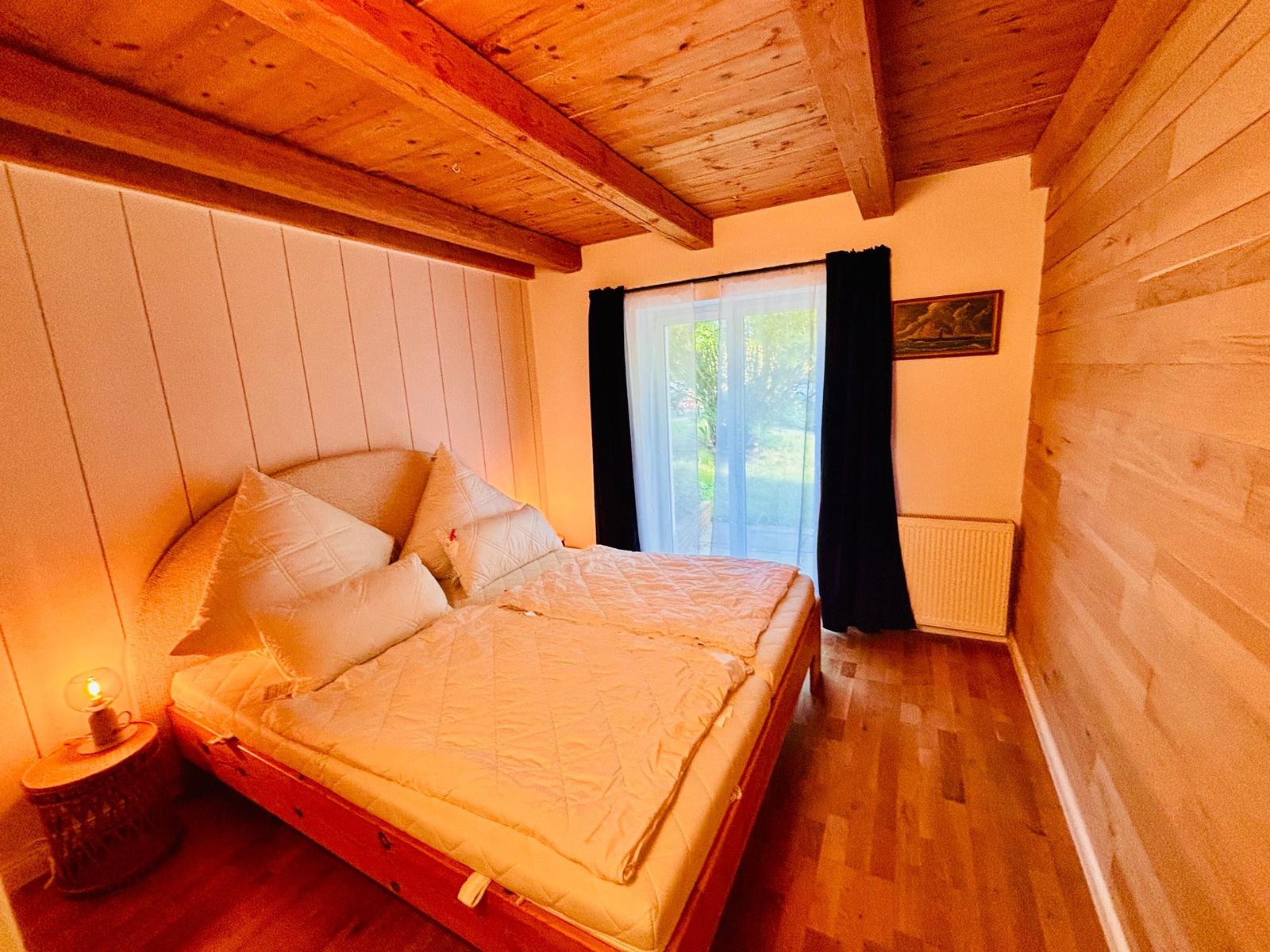 Schlafzimmer mit Holzboden, Bett und Fenster. Decke mit Balken.