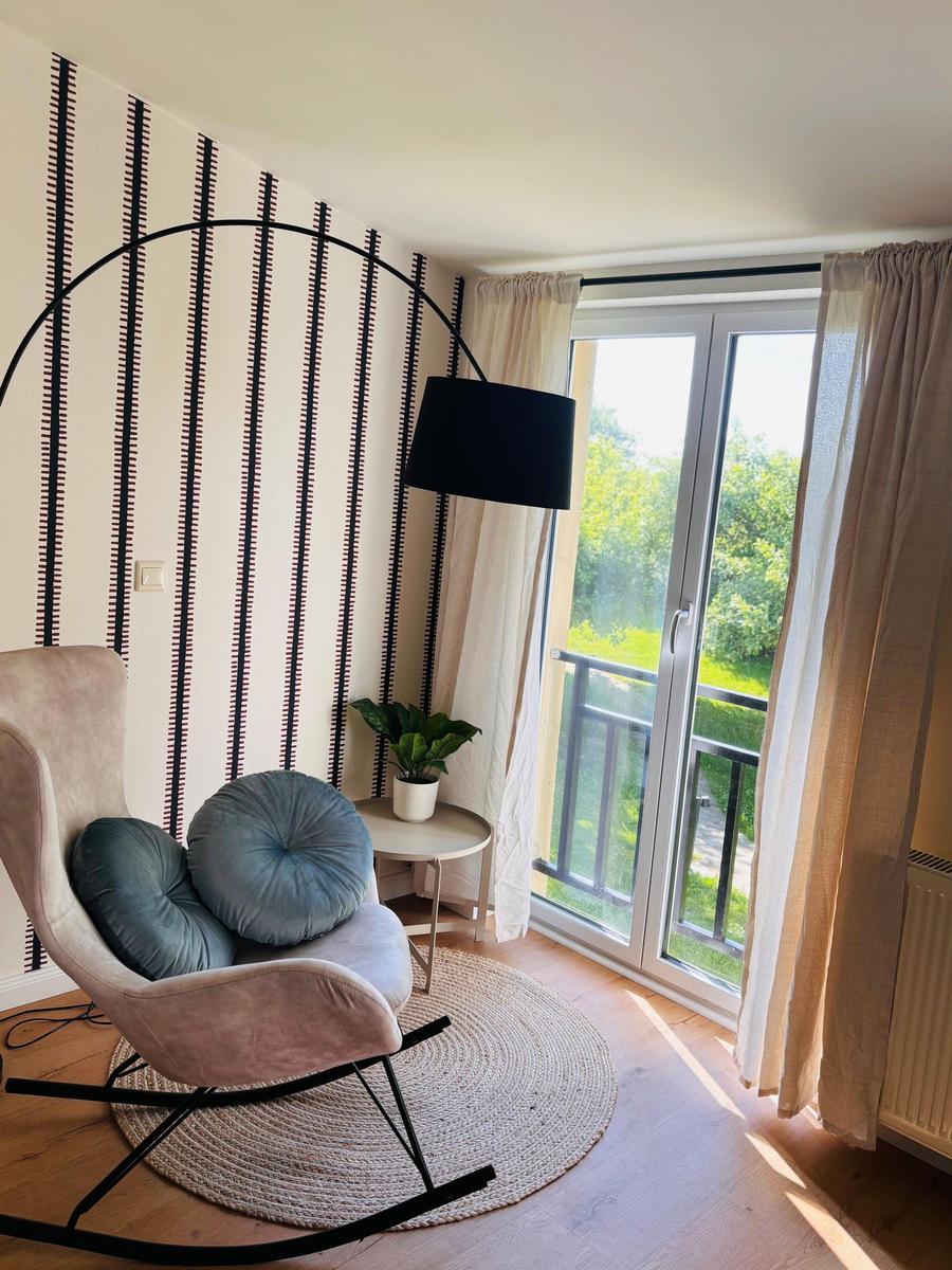 Ein Raum mit einem Sessel, einer Lampe und einer Glastür zum Balkon.