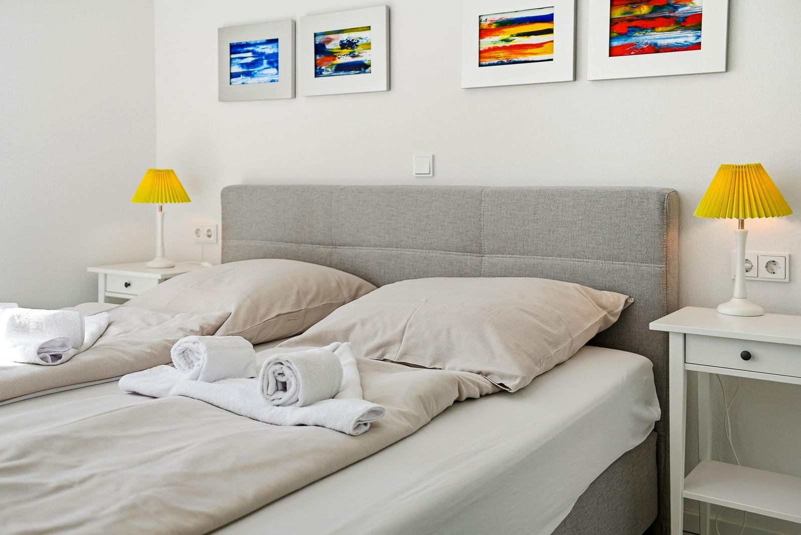 Ein Bett mit Kissen und Handtüchern, zwei Nachttische mit Lampen und Wandbildern.