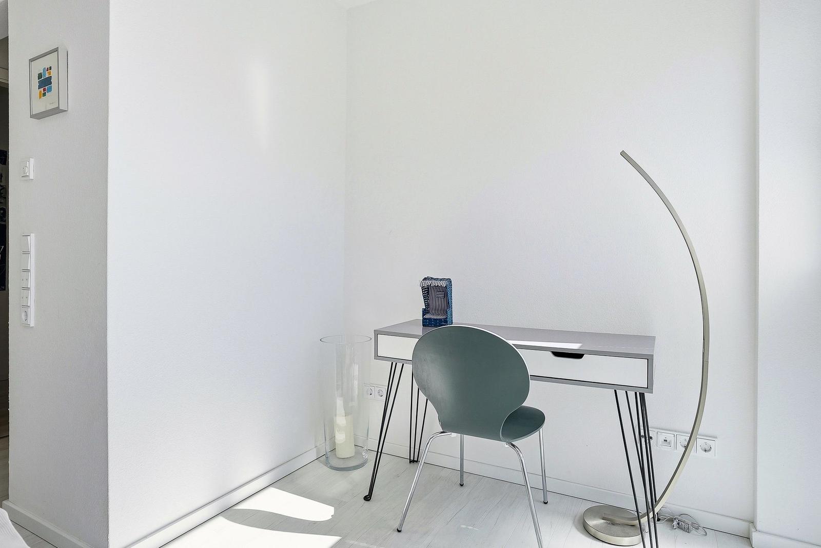 Schreibtisch mit Stuhl und Stehlampe in einem hellen Raum.