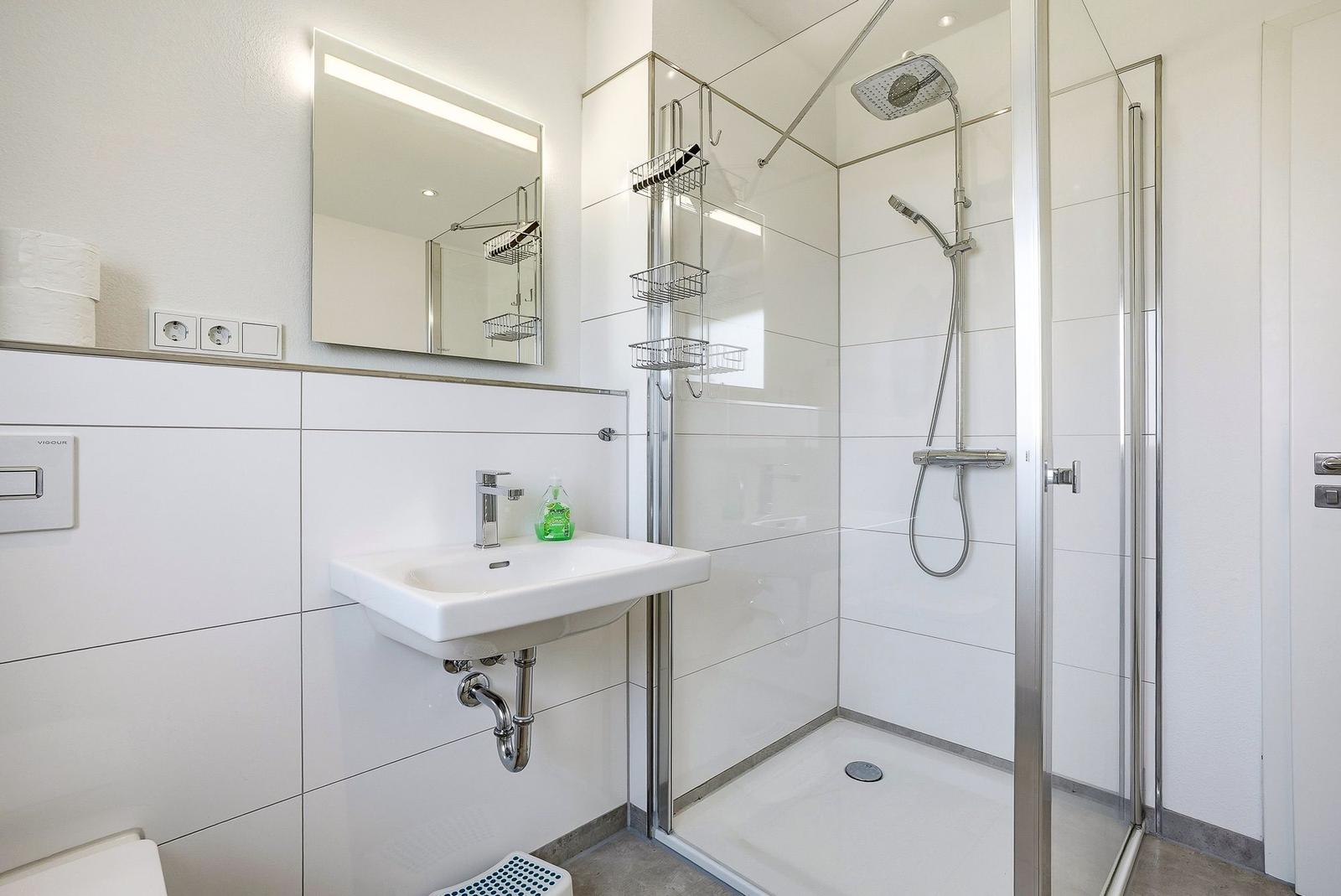 Badezimmer mit Dusche, Waschbecken und Spiegel. Fliesenwand und modernes Design.