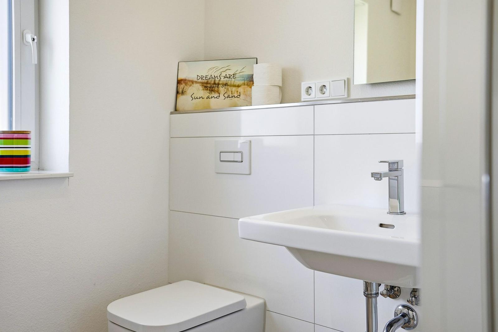 Badezimmer mit Waschbecken, Spiegel und Toilette. Fenster mit buntem Behälter.