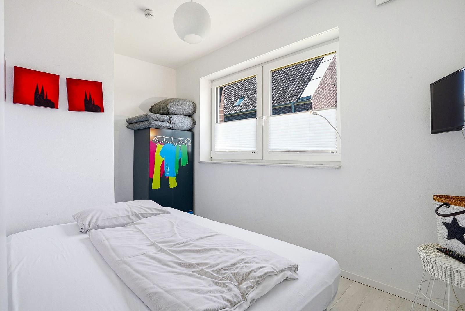 Schlafzimmer mit Bett, Kleiderschrank und Fenster mit Blick auf Dächer.