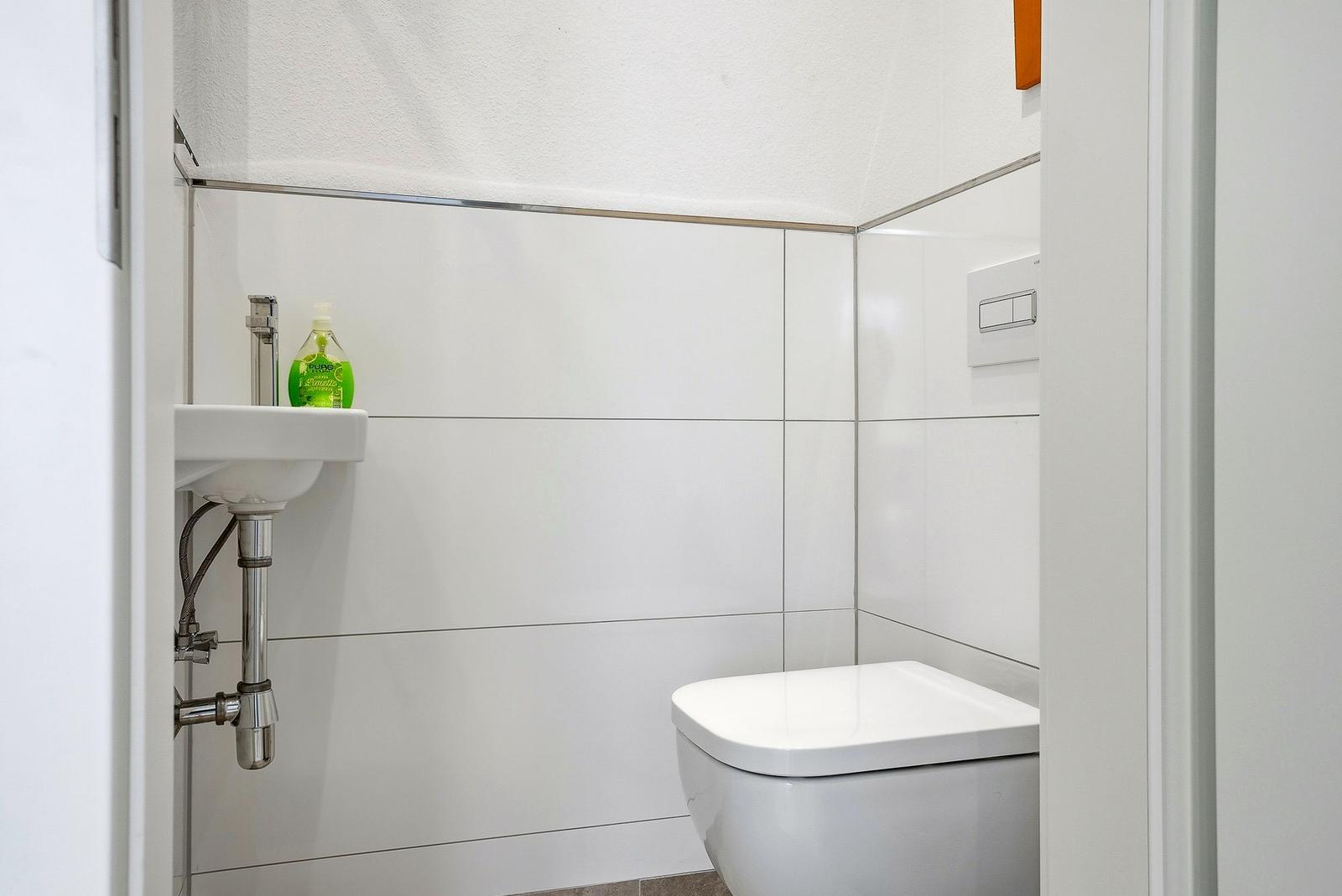 Badezimmer mit Toilette und Waschbecken mit grünem Seifenspender.