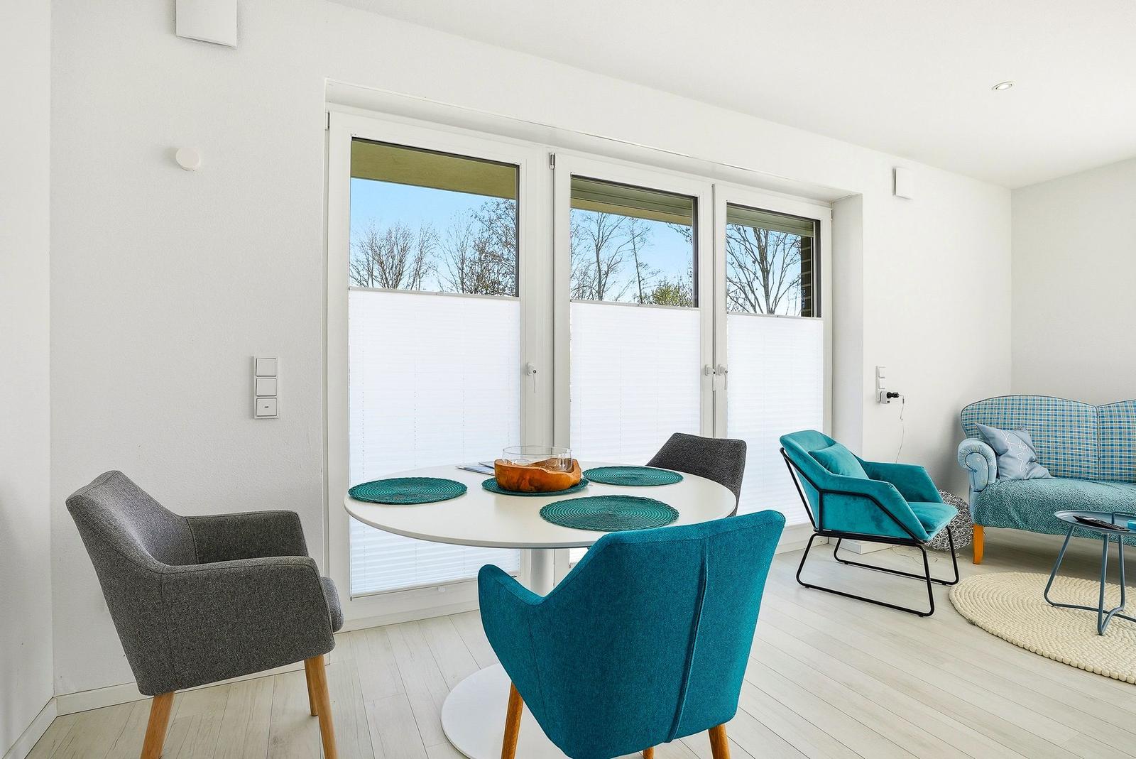 Essbereich mit runden Tisch und Stühlen, große Fenster, Sofa und Sessel im Hintergrund.