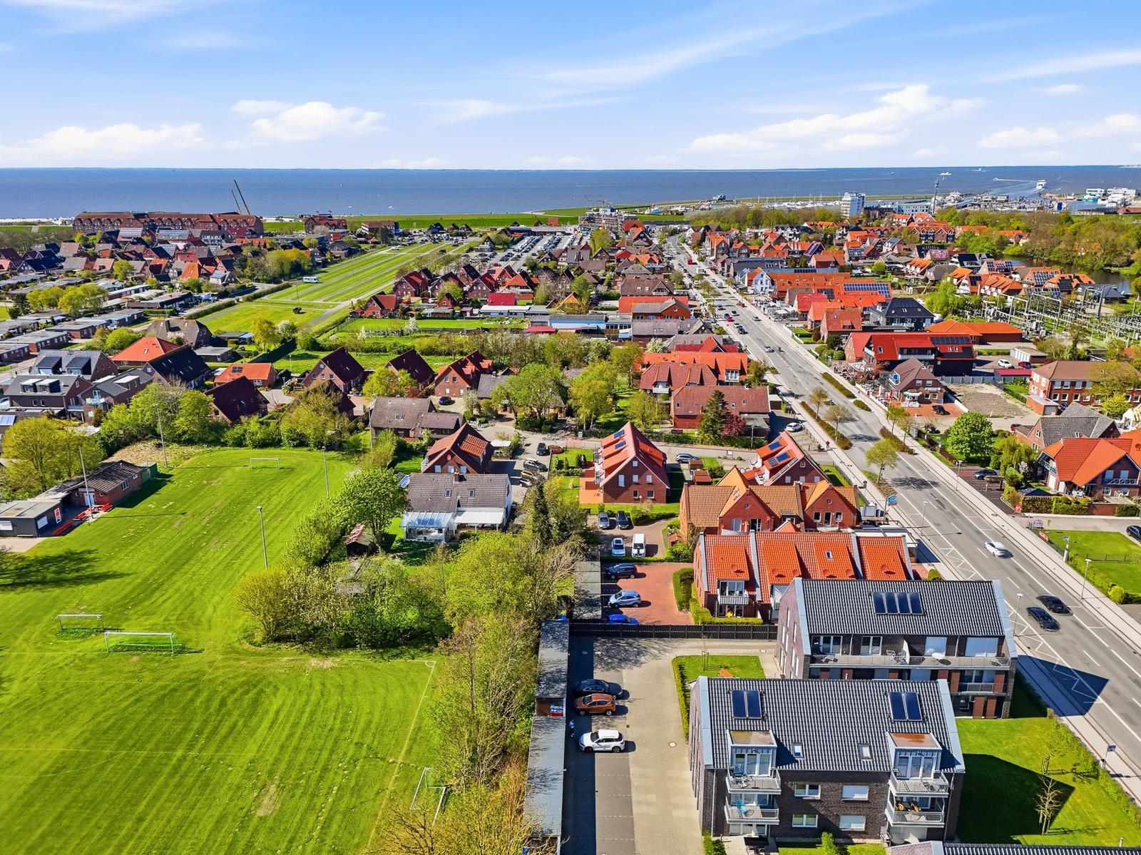 Aerial view of a coastal town with red-roofed houses, green fields, and the sea in the background.