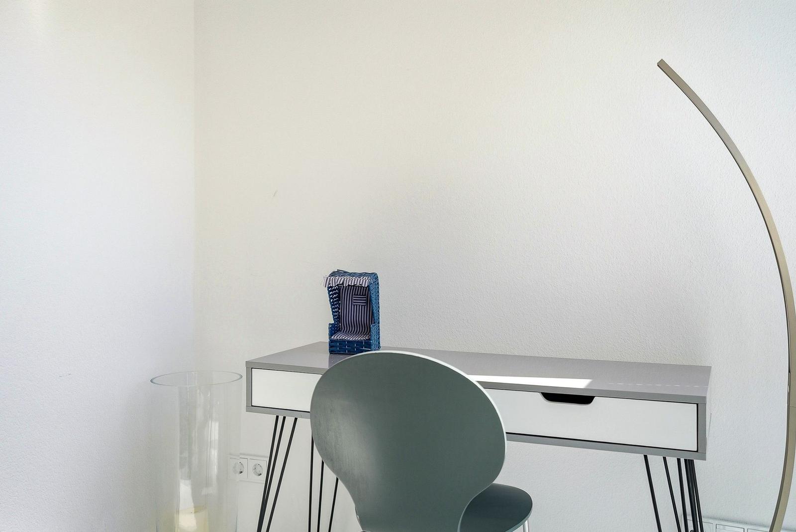 Schreibtisch mit Stuhl und Stehlampe in minimalistischem Raum.