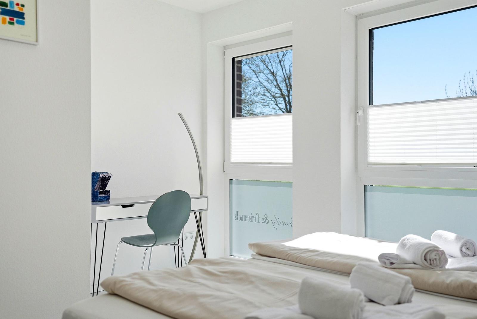 Schlafzimmer mit Bett, Schreibtisch und Fenster mit Jalousien.
