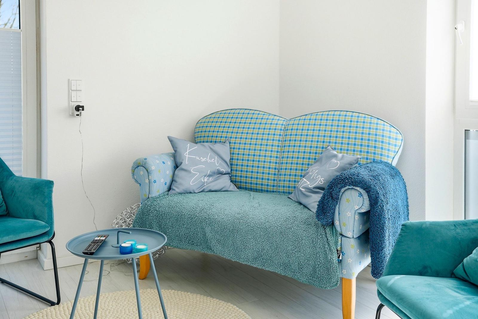 Ein Sofa mit kariertem Stoff und blauer Decke. Zwei Kissen und zwei Sessel sind sichtbar.