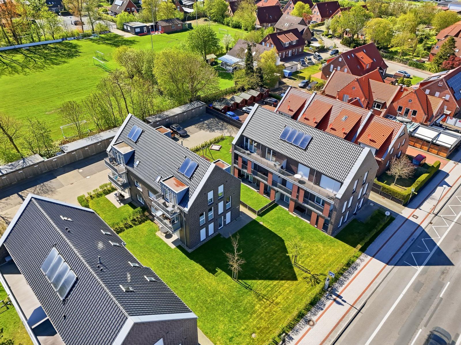 Modernes Mehrfamilienhaus mit Solaranlagen und Garten. Blick auf Wohngebiet mit Sportplatz.