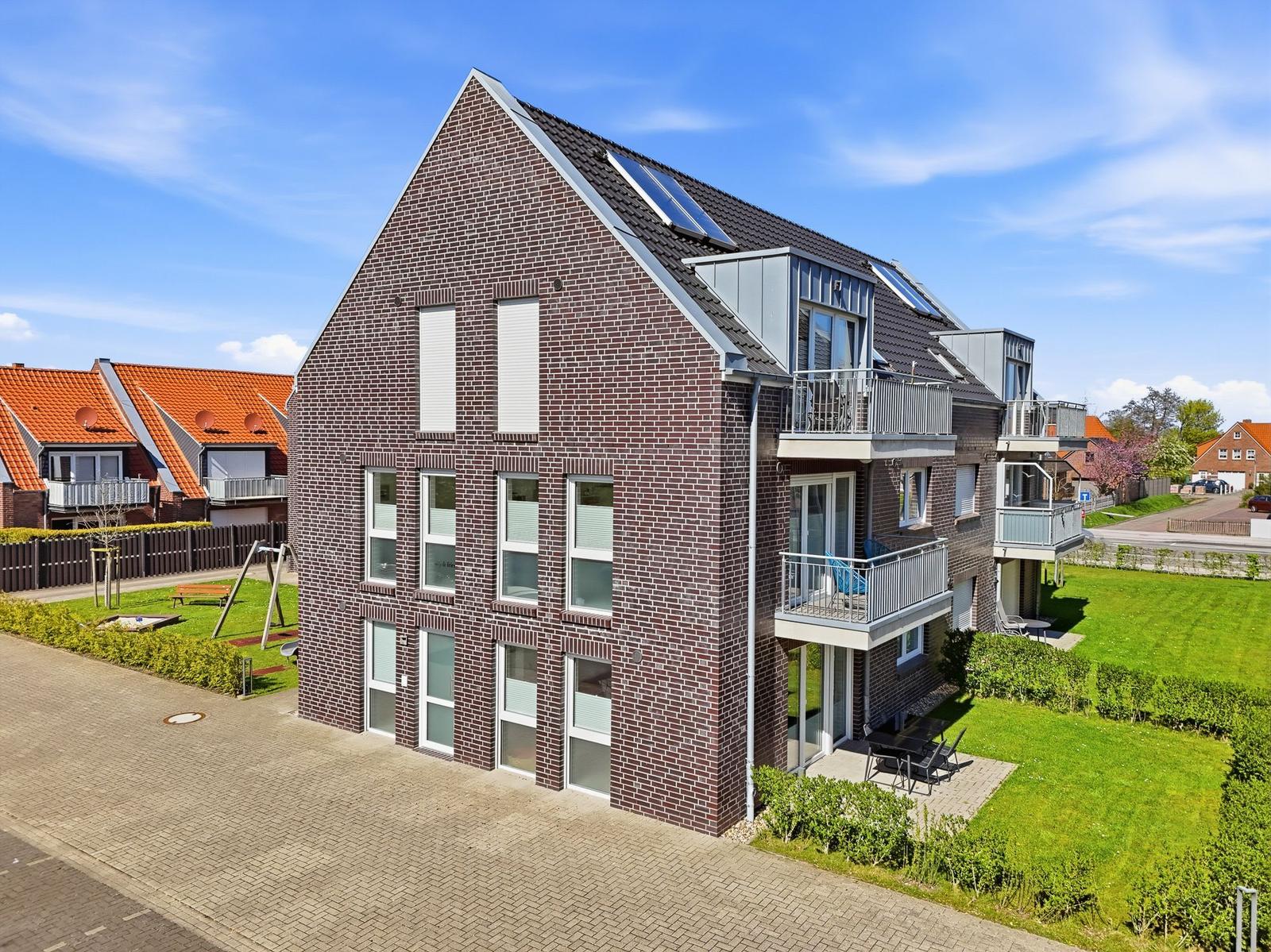 Moderne Mehrfamilienhaus mit Balkonen und Gartenbereich unter blauem Himmel.