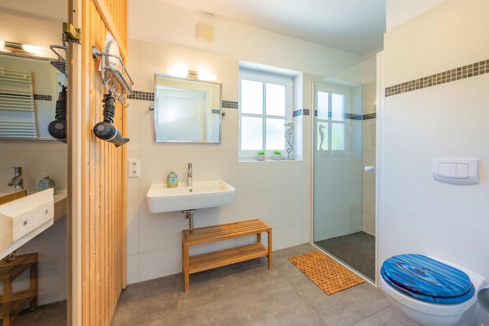 Badezimmer mit Dusche, Waschbecken und Toilette. Holzbank und blauer Sitz.