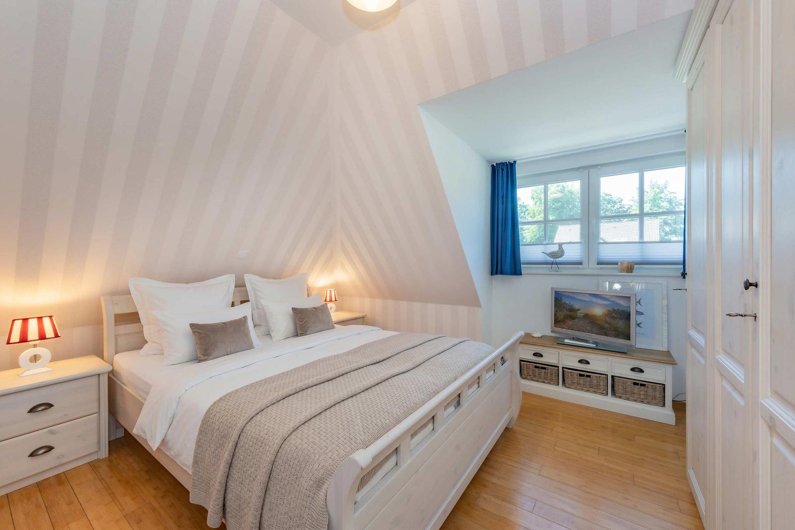 Schlafzimmer mit Bett, Nachttisch, TV und Fenster mit blauen Vorhängen.