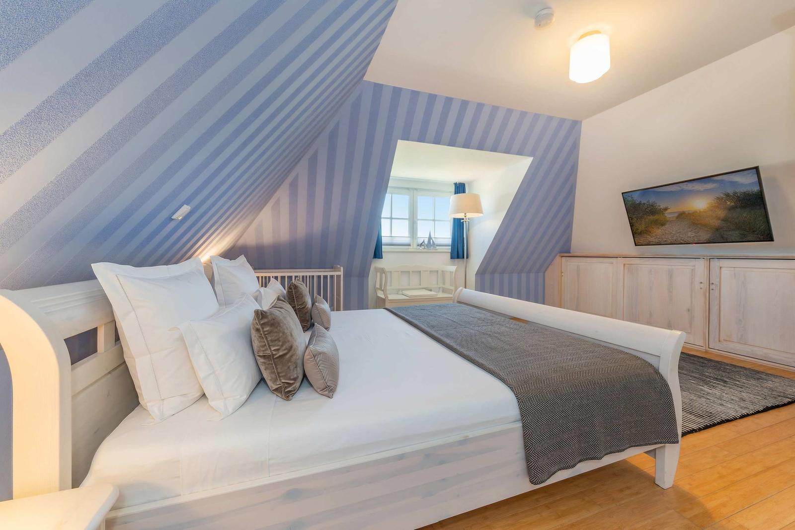 Schlafzimmer mit Dachschrägen, Bett, Fernseher und Fenster