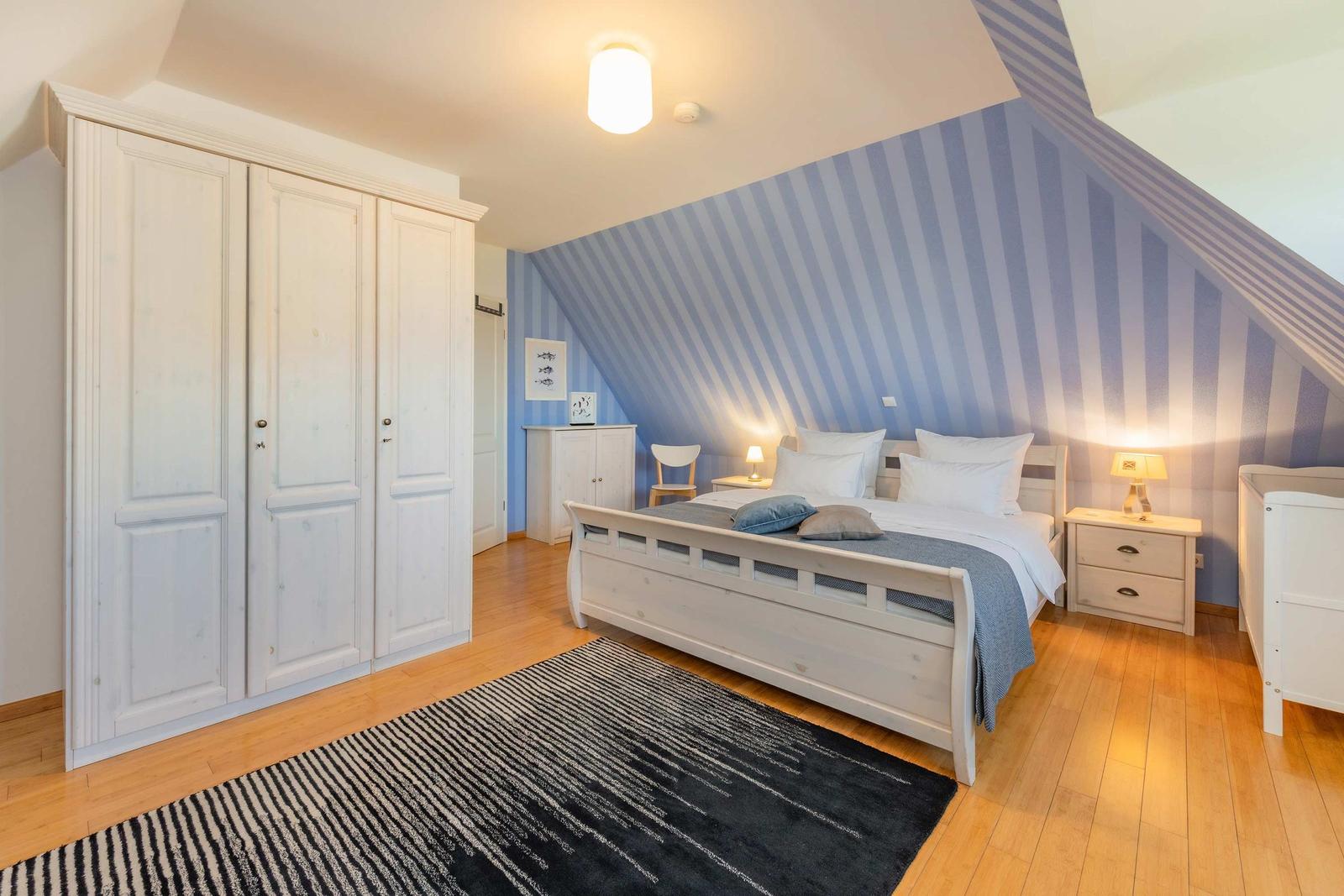 Schlafzimmer mit Bett, Kleiderschrank und gestreifter Wand