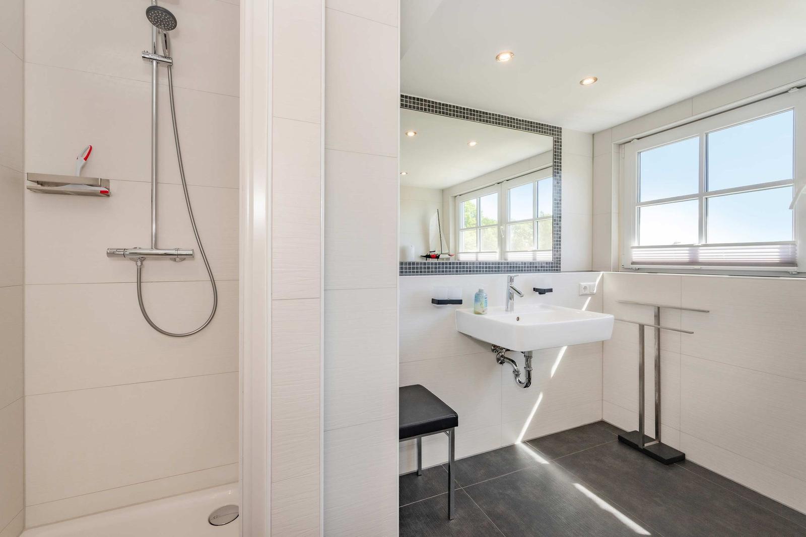 Badezimmer mit Dusche, Waschbecken und Fenster.