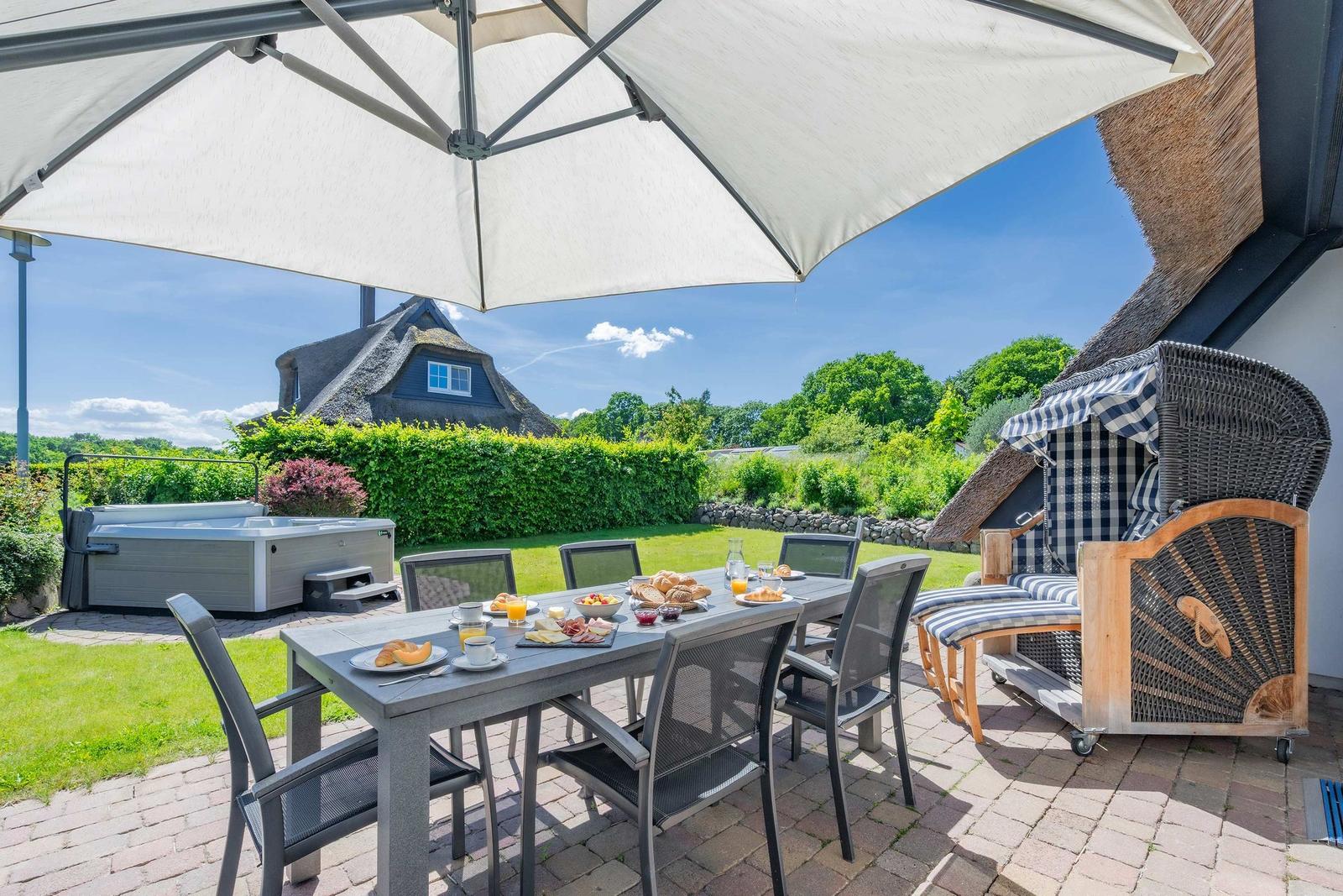 Terrasse mit Tisch, Stühlen und Sonnenschirm. Im Hintergrund Badewanne und Grünanlage.