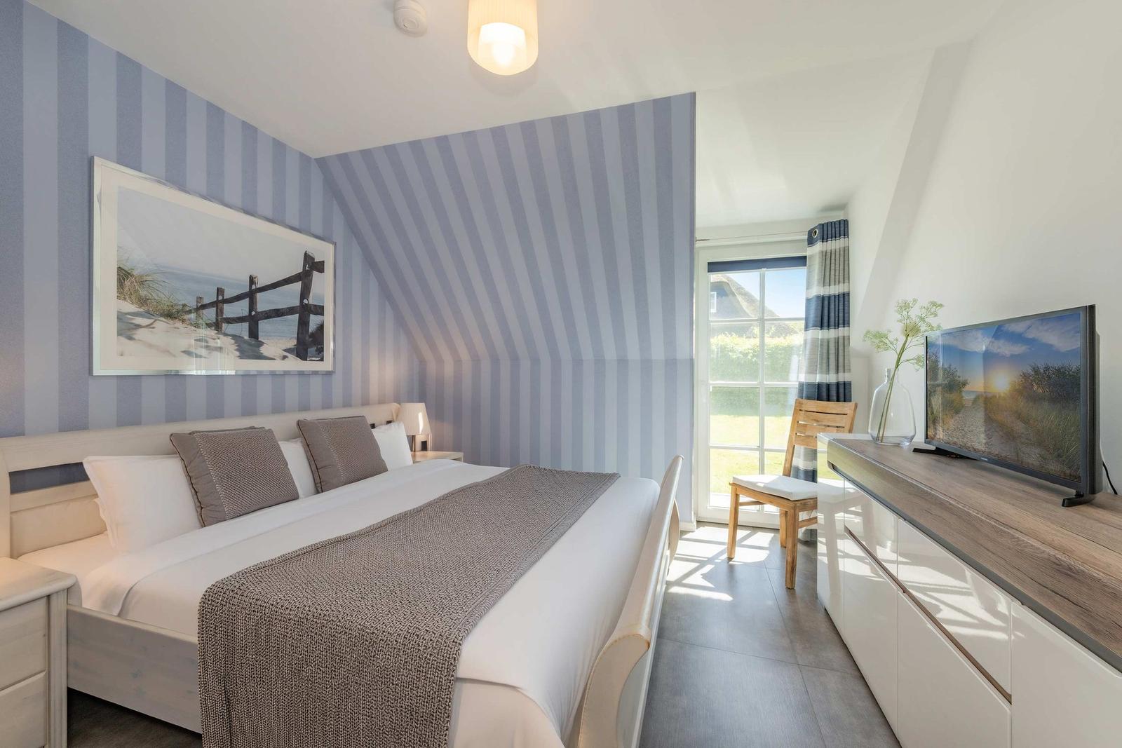 Schlafzimmer mit Bett, Fernseher und Fenster zum Garten