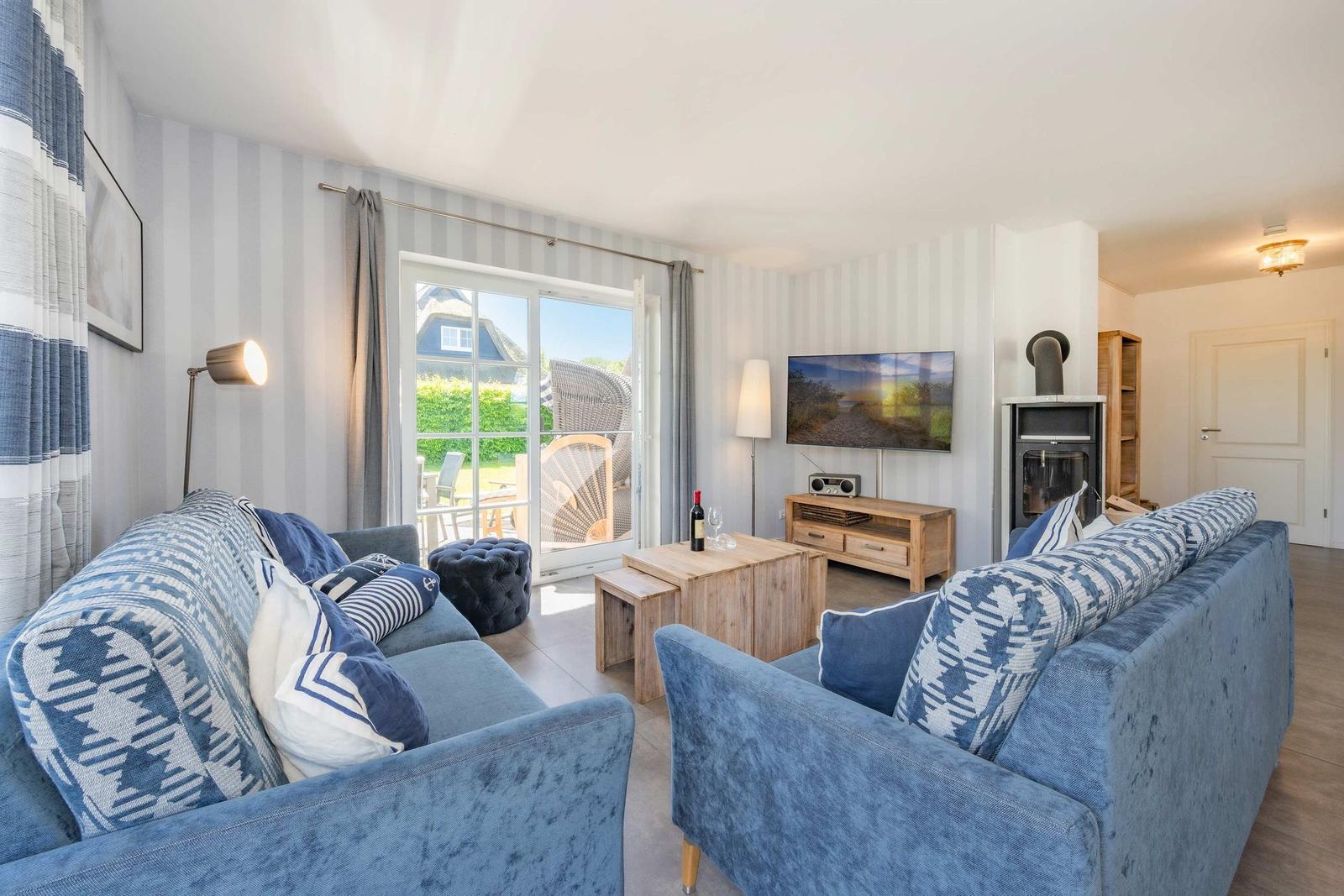 Wohnzimmer mit blauen Sofas, Fernseher und Kamin. Durchgang zur Terrasse mit Gartenansicht.