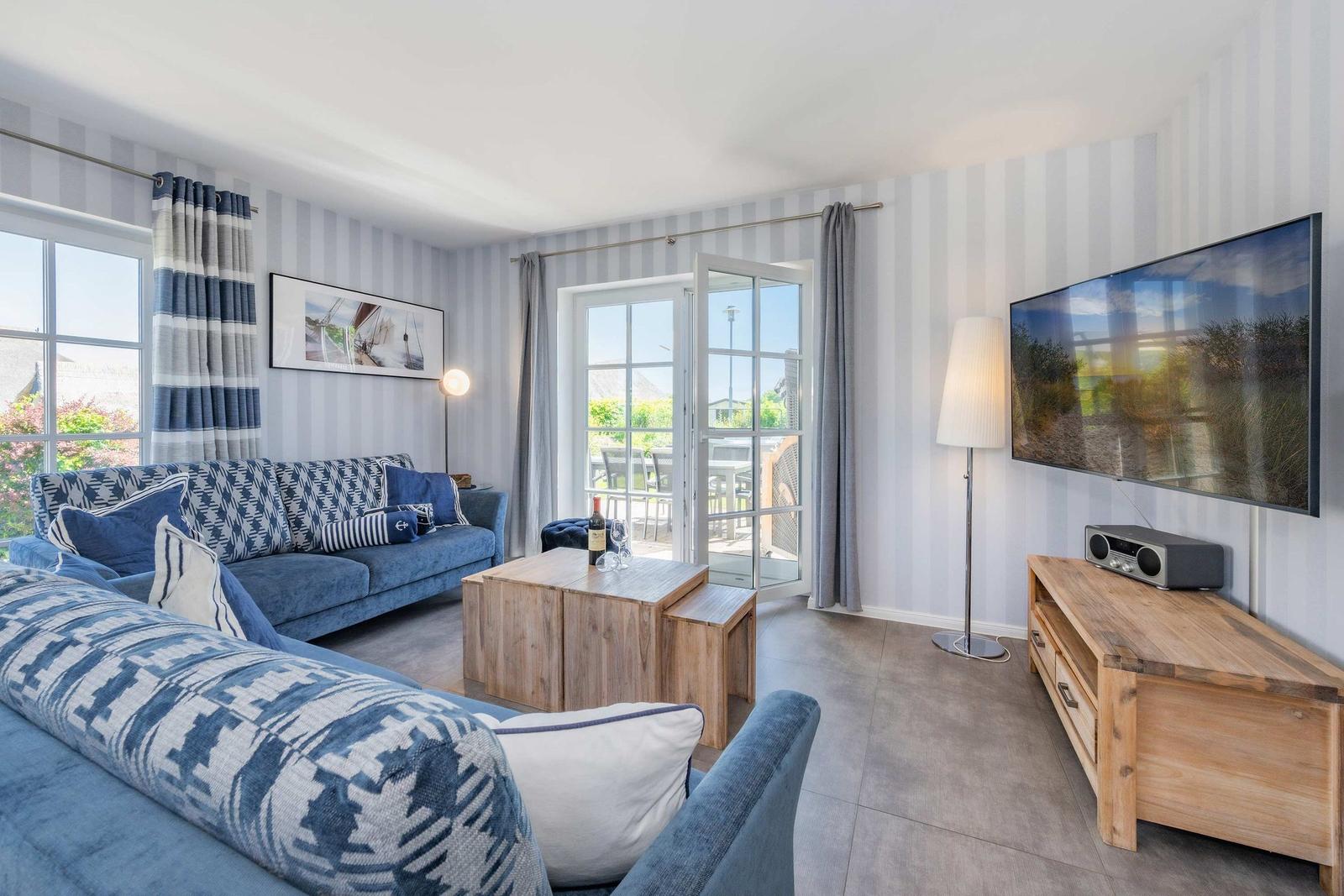 Ein Wohnzimmer mit blauem Sofa, Holztisch und Fernseher an der Wand.