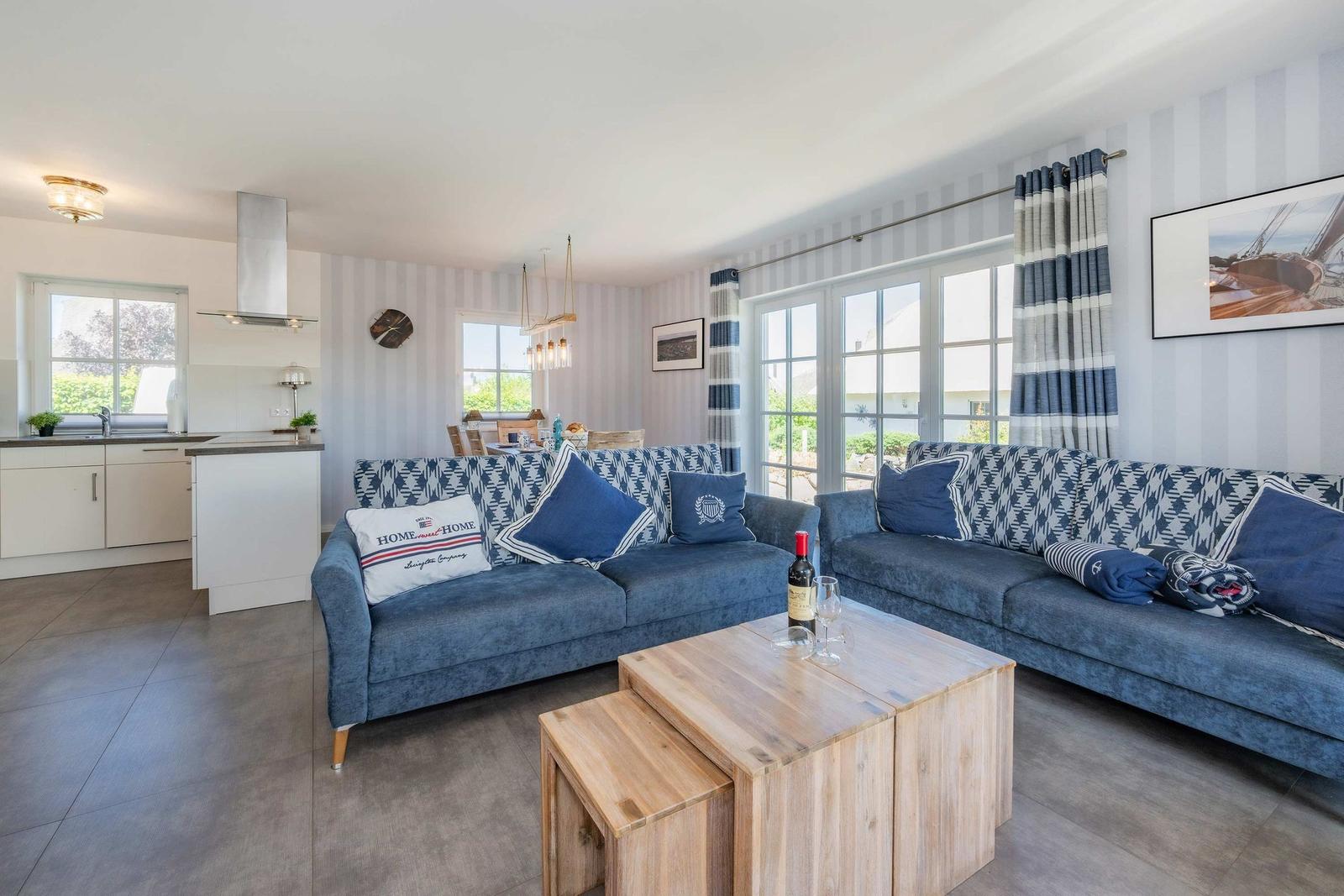 Wohn- und Küchenbereich mit blauen Sofas, Holztisch und Fenstern.