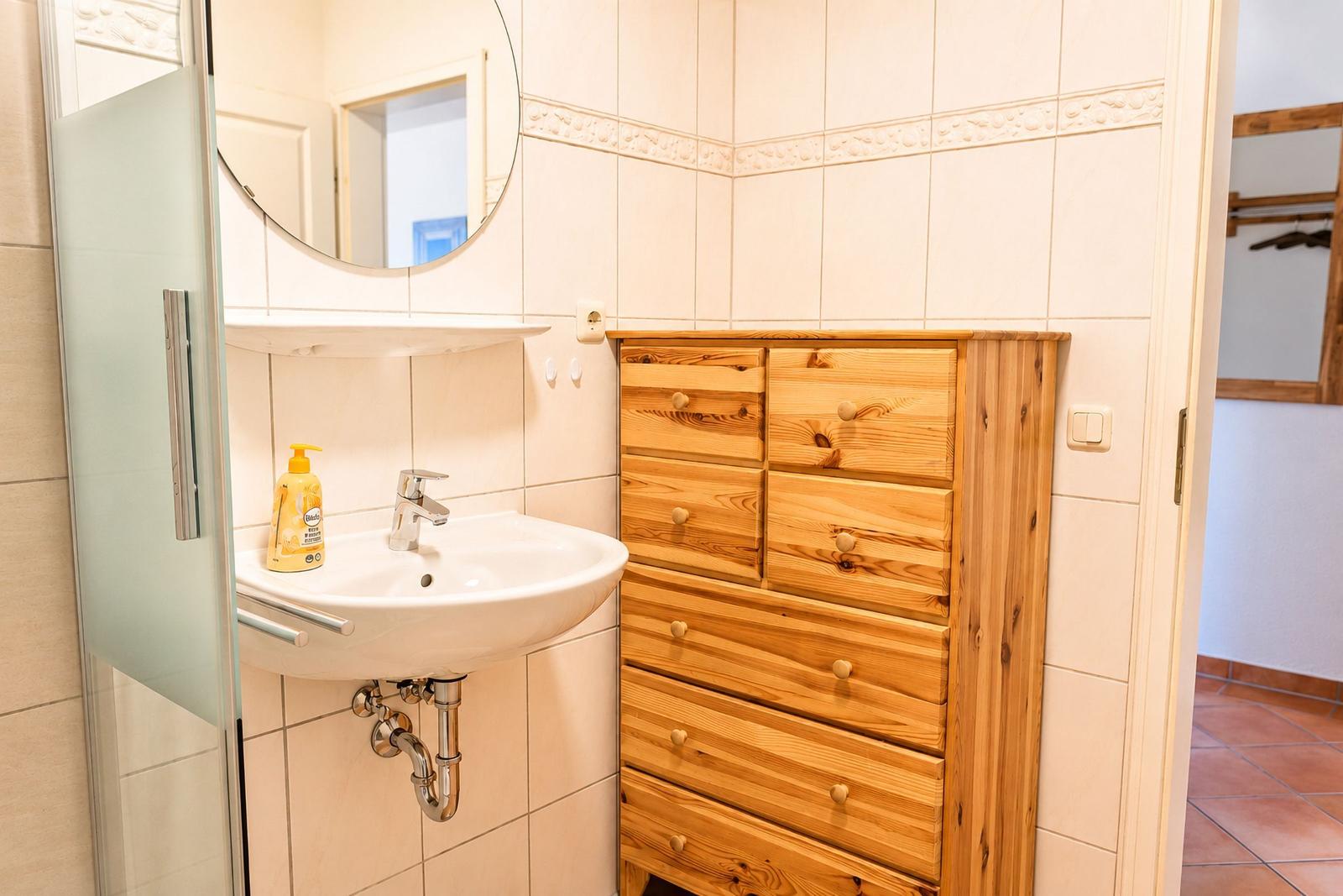 Badezimmer mit Waschbecken, Spiegel und Holzschrank.