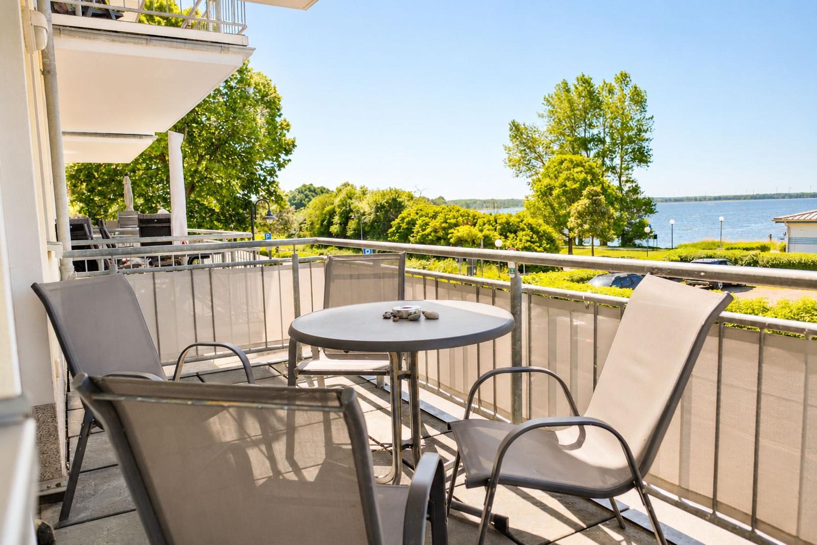 Terrasse mit Tisch und Stühlen, Blick auf Wasser und Bäume.