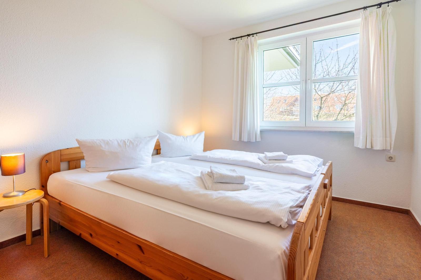 Schlafzimmer mit Holzbett, Fenster und Nachttisch.