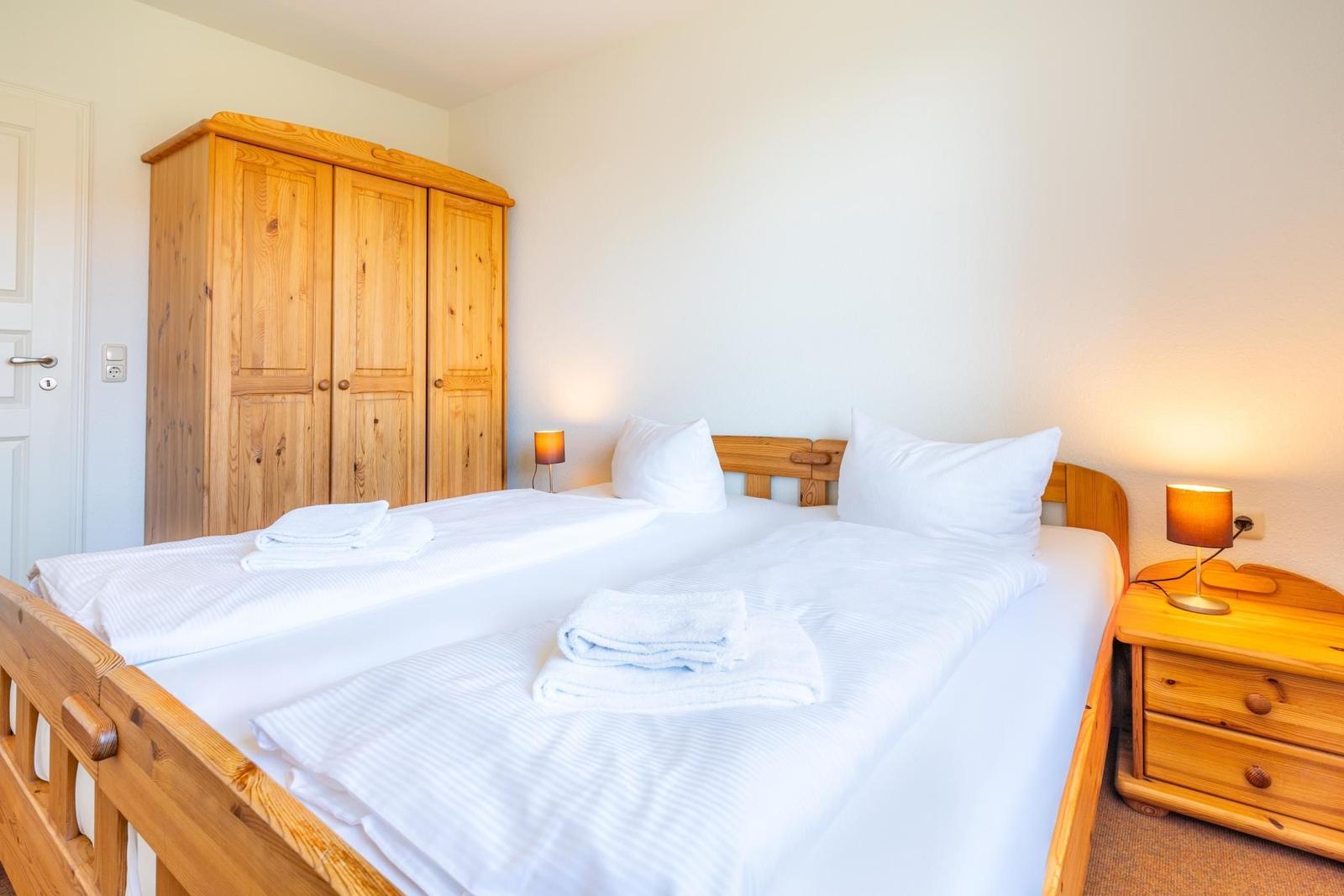Schlafzimmer mit Holzbett, Kleiderschrank und Nachttisch mit Lampen.