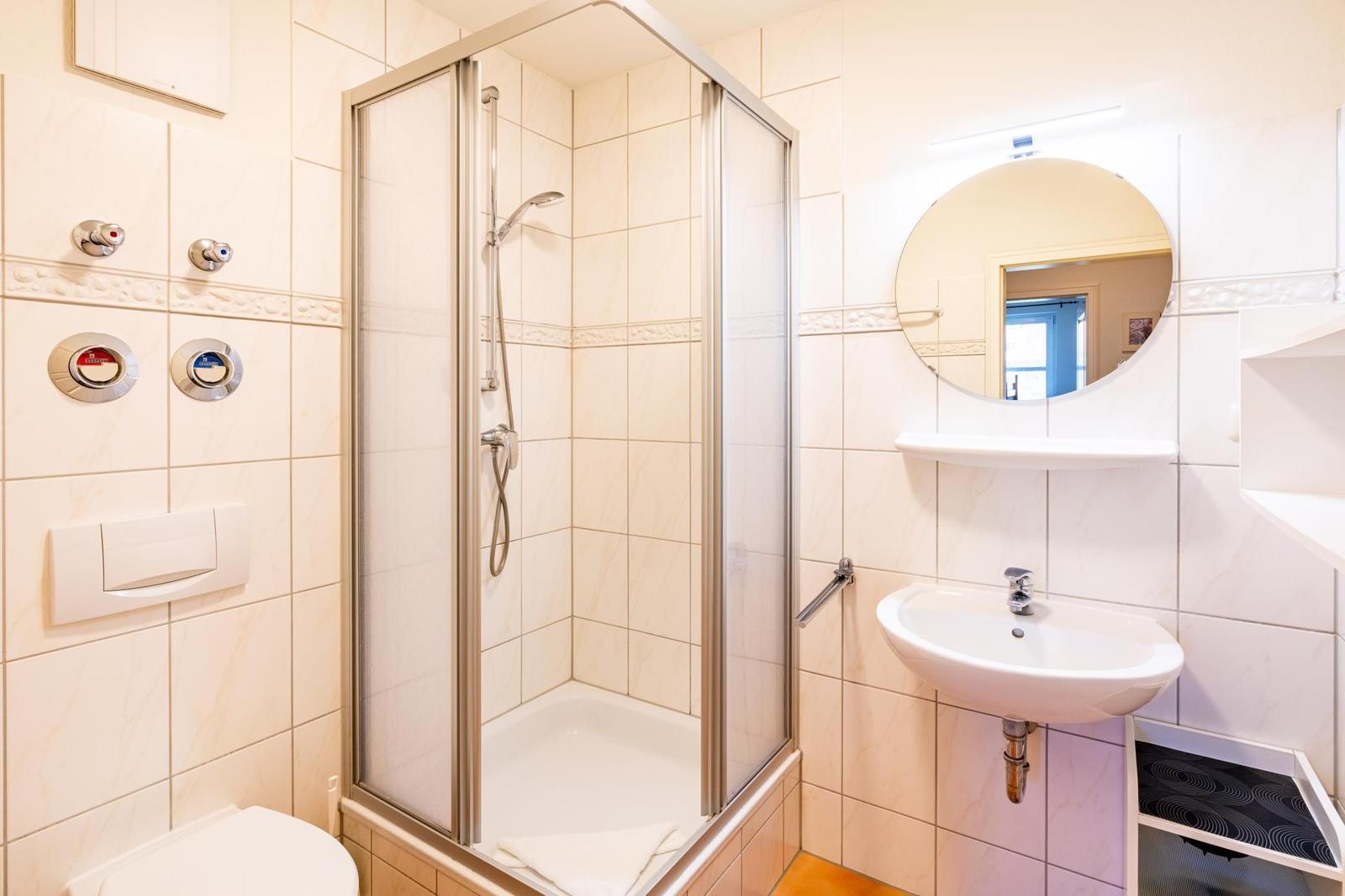 Badezimmer mit Dusche, Waschbecken und Spiegel.