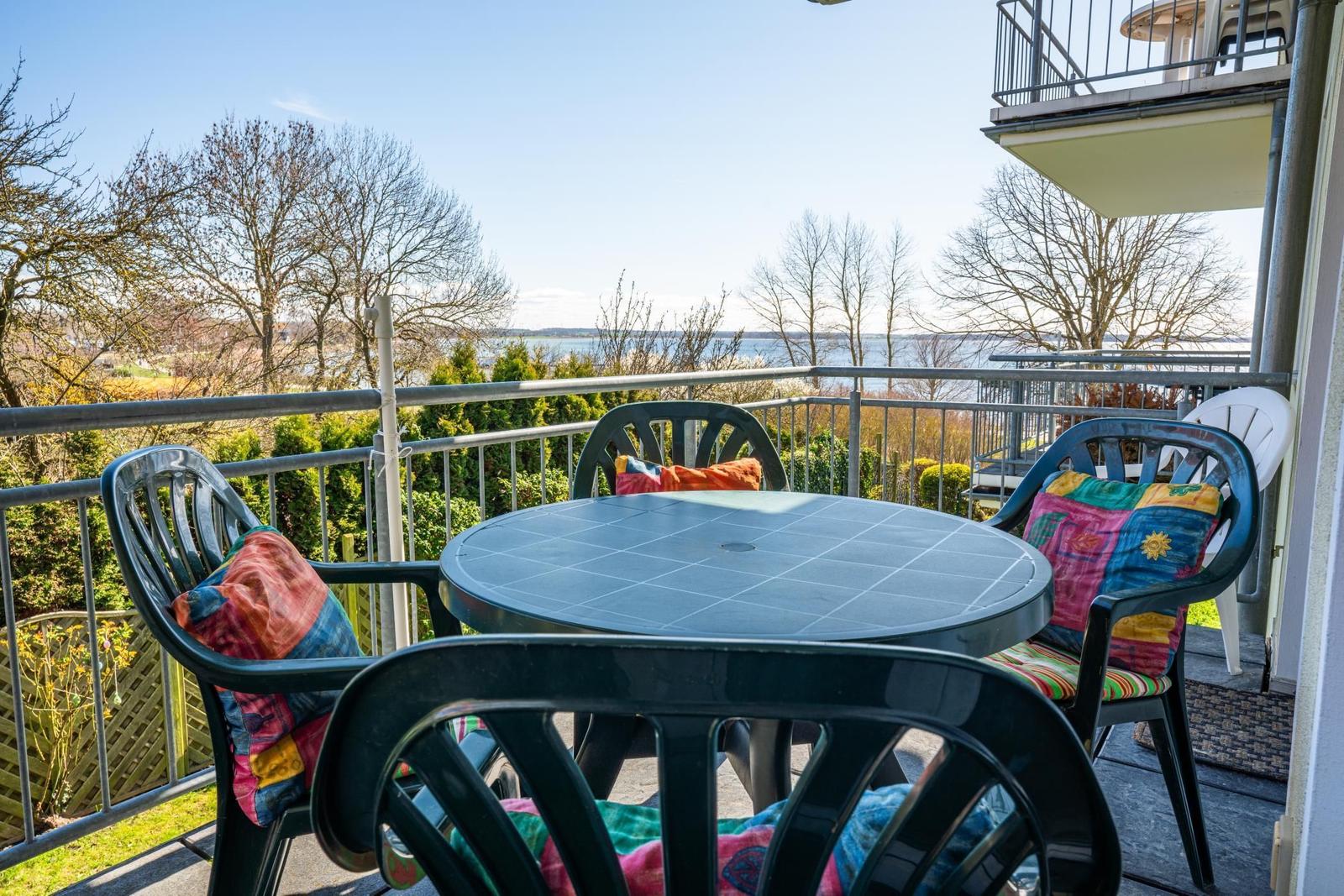 Terrasse mit Tisch und Stühlen, Blick auf Wasser und Bäume.