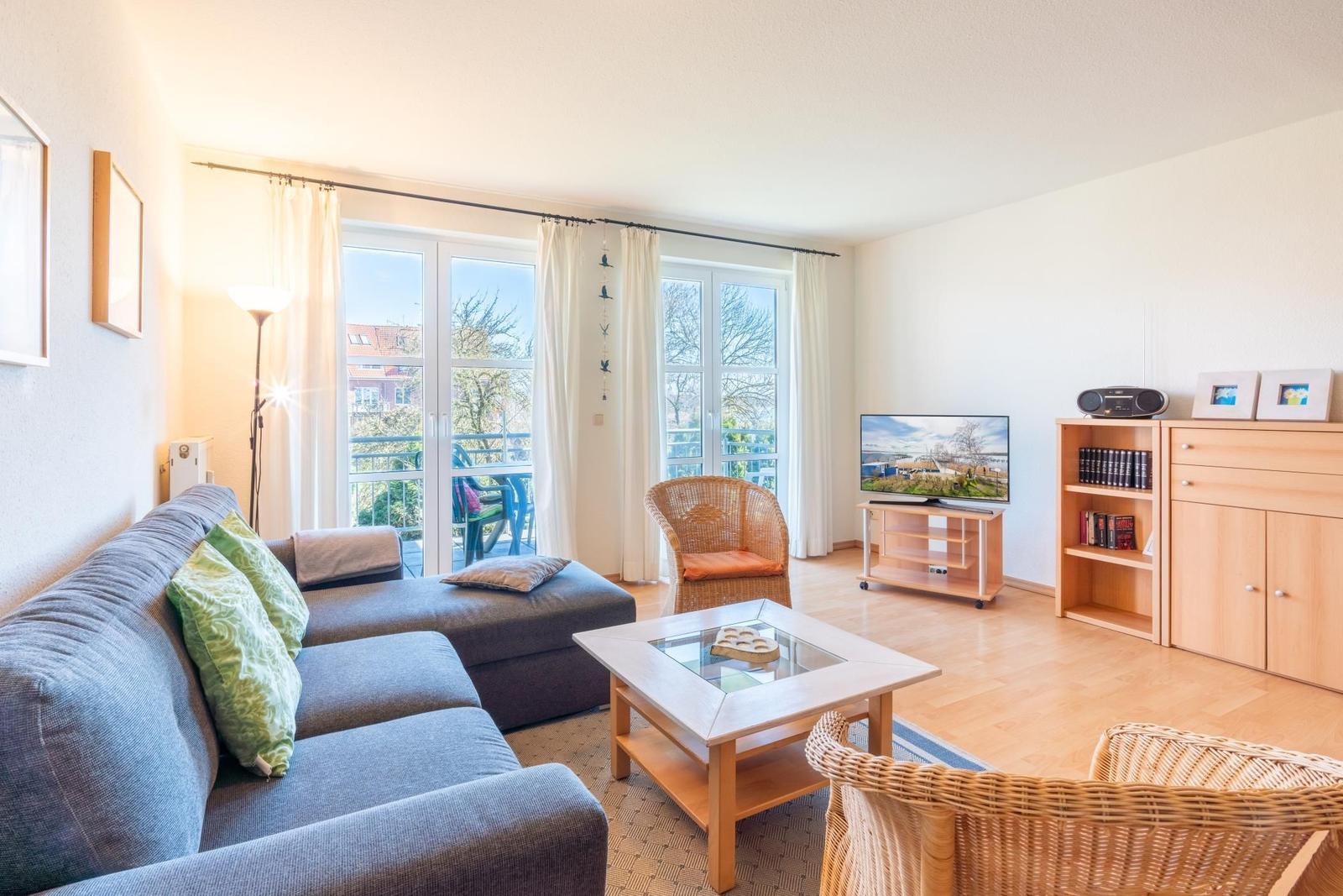Wohnzimmer mit Sofa, Esstisch, Fernseher und Balkonansicht.