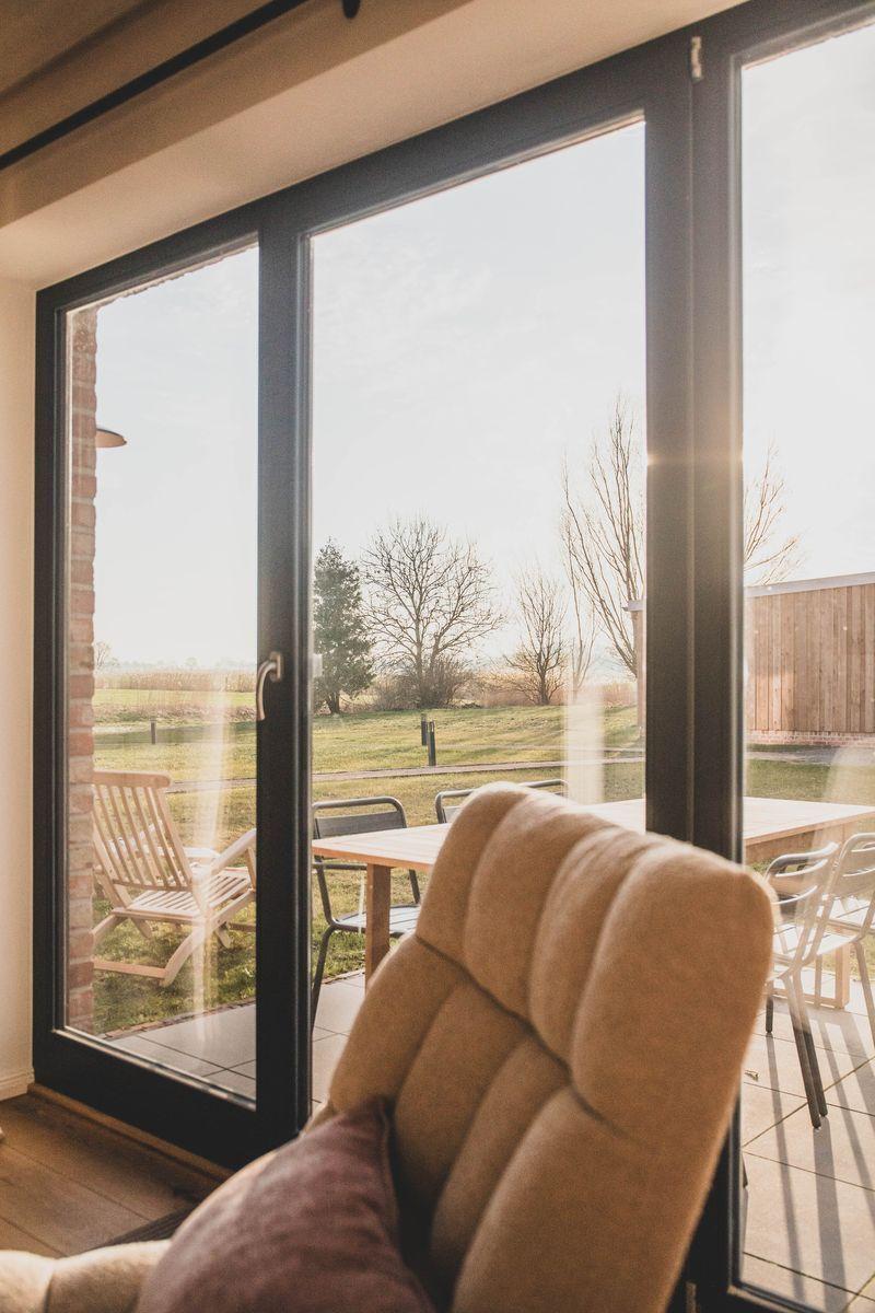 Ein Sessel vor großen Fenstern mit Blick auf eine Terrasse und Landschaft.