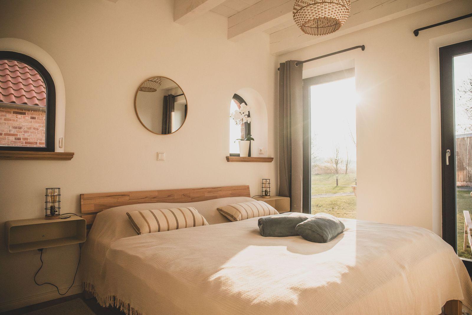 Schlafzimmer mit Bett, runden Spiegel und Fenster zum Garten
